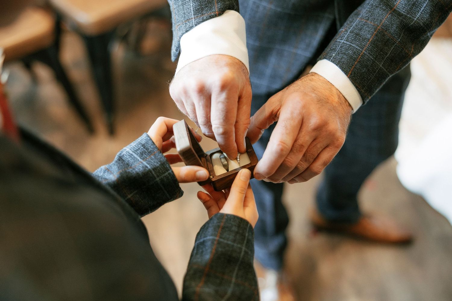 Two men in suits exchanging wedding rings in a wooden box during a wedding ceremony preparation.