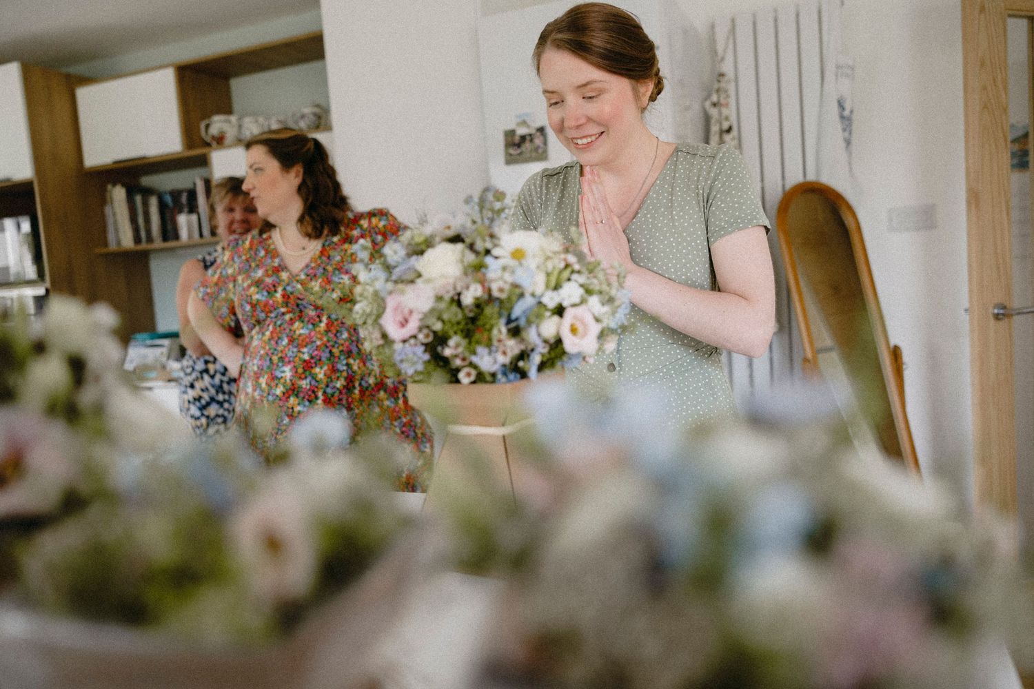 Two women arranging fresh floral bouquets with pastel flowers in a bright, cozy interior space.