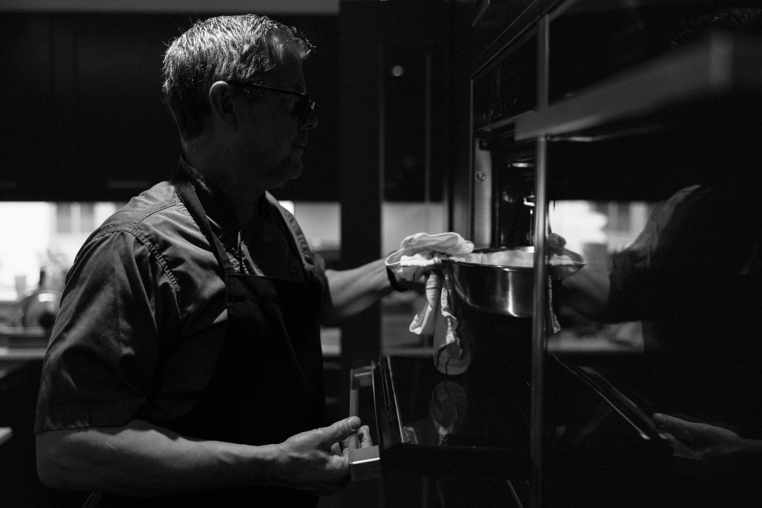 Black and white photo of a chef cleaning kitchen equipment in a professional restaurant kitchen.