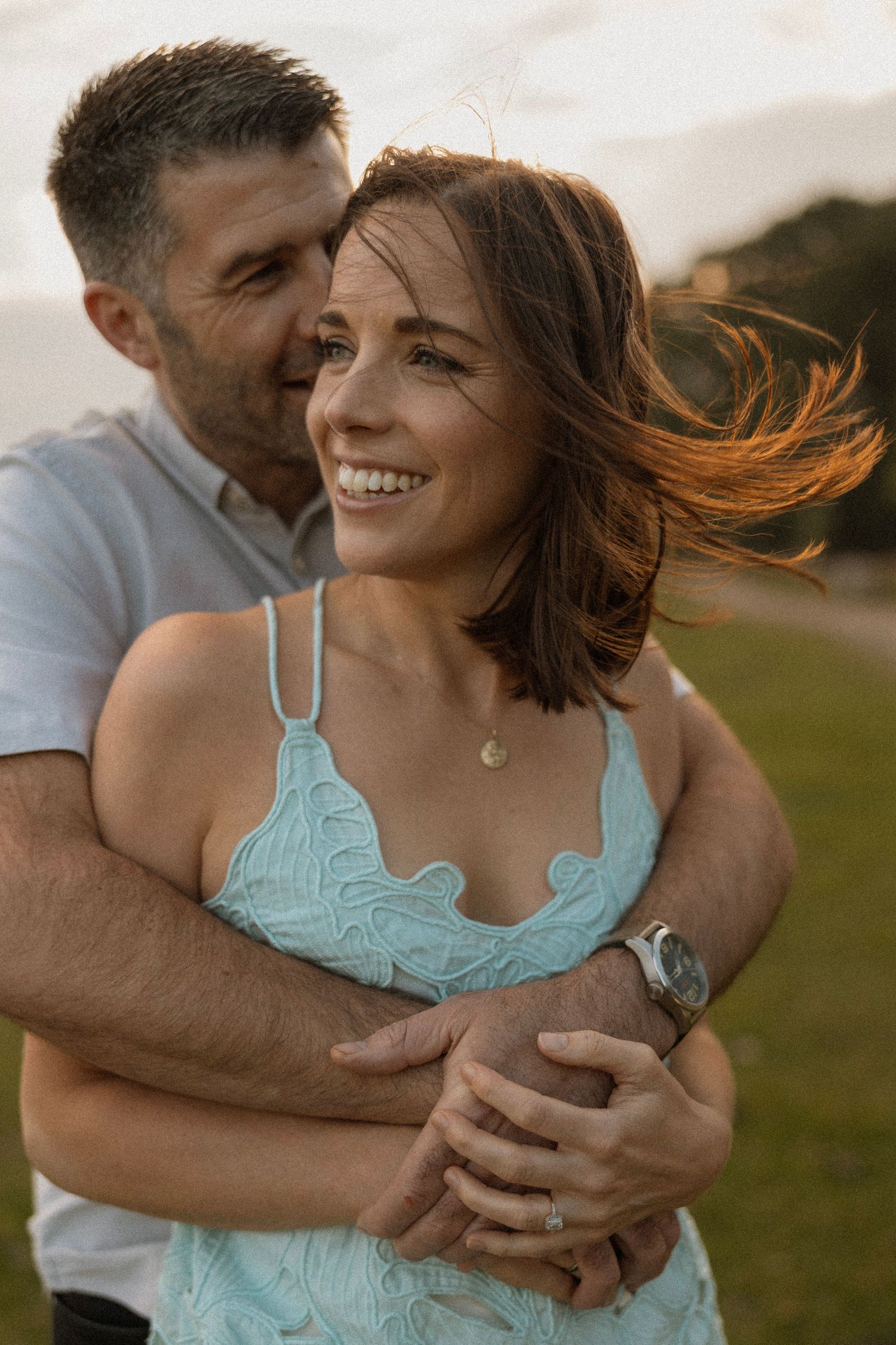 Couple embracing in warm sunset light with wind blowing through hair.