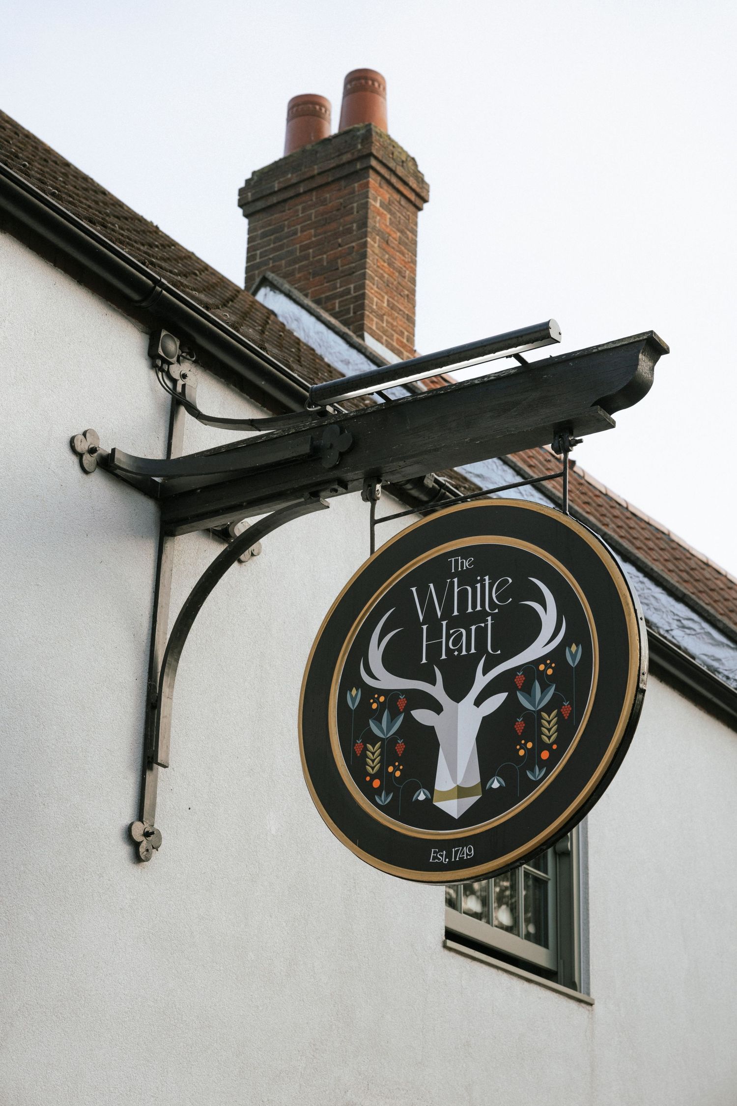 The White Hart pub sign featuring a white stag on a dark circular board, mounted on a bracket outside a white building.