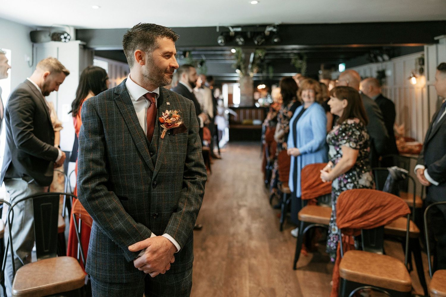 A guest in formal tweed attire stands in a restaurant venue during an event.