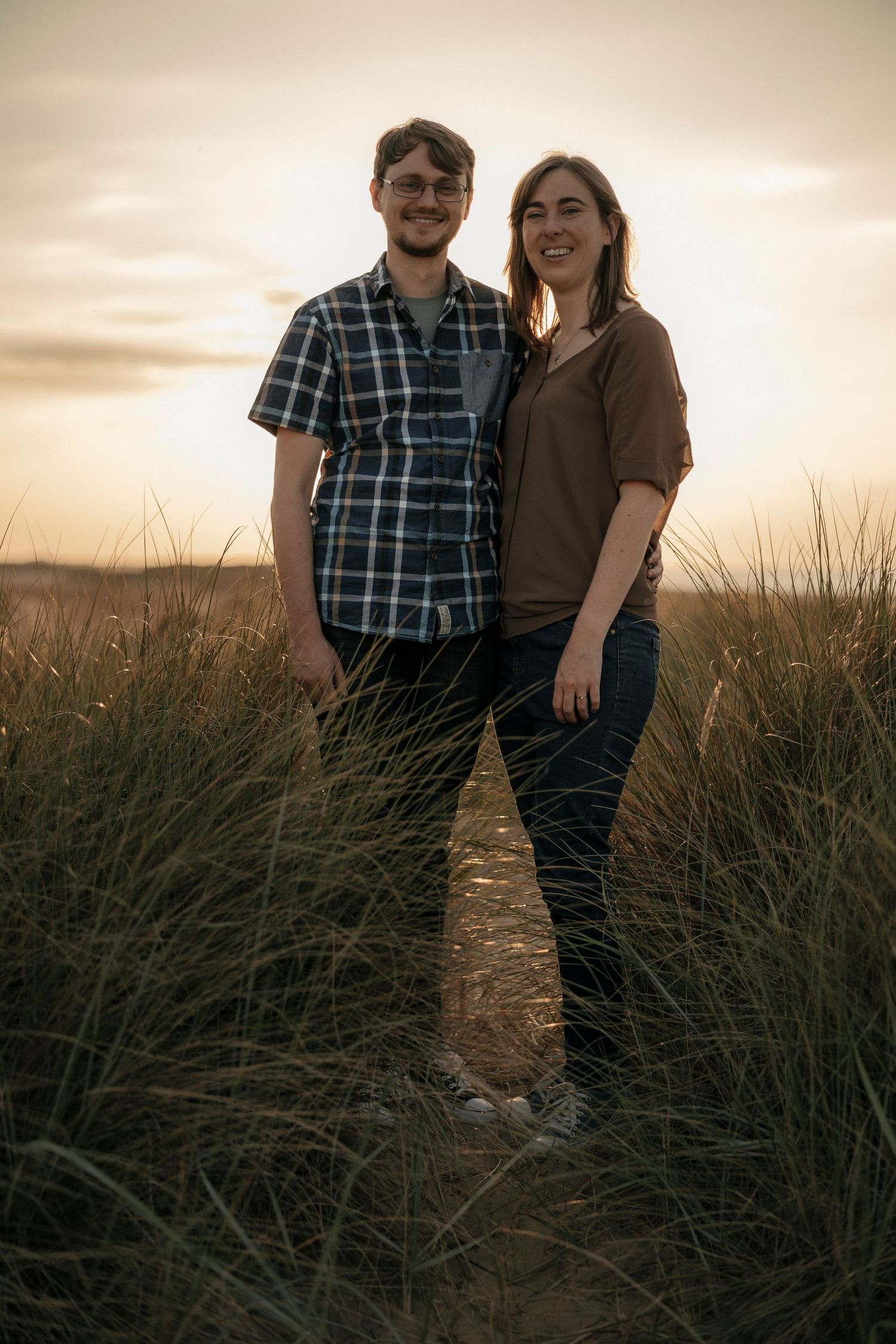 Couple smiling together in tall grass at golden sunset.