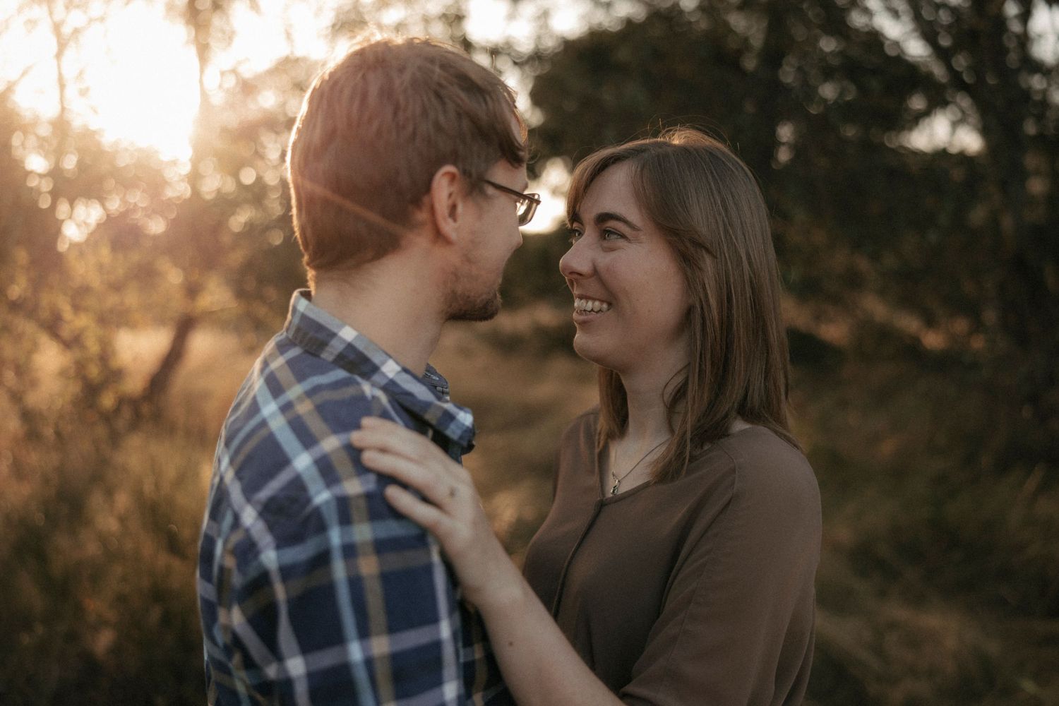 Couple sharing a romantic moment at golden hour in a field, woman smiling joyfully.