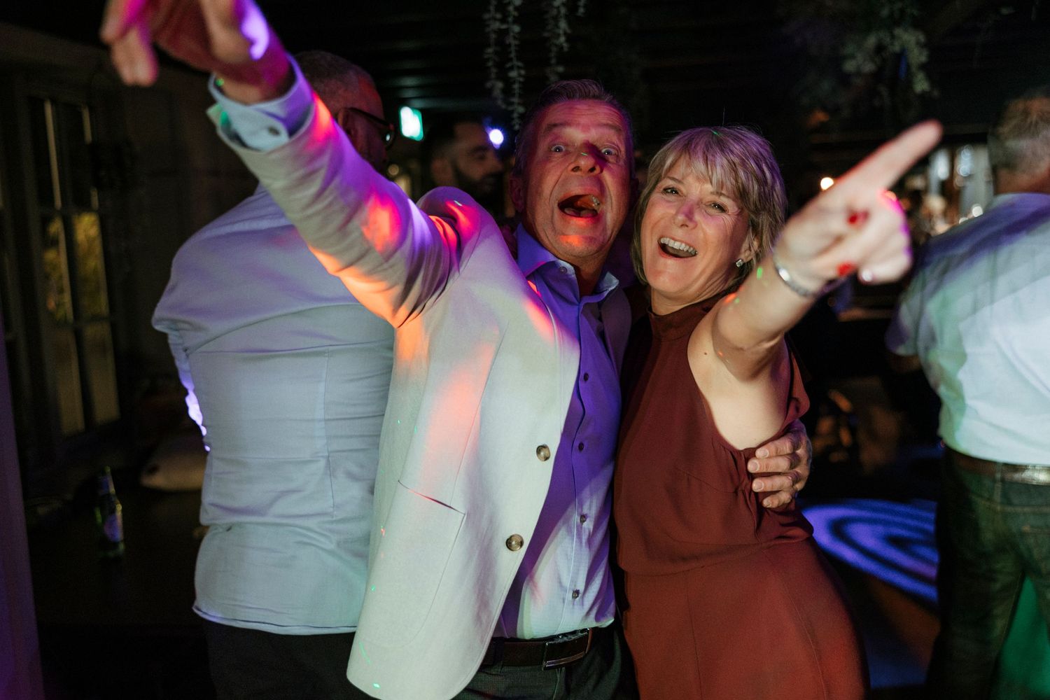 Joyful couple dancing under colorful party lights at nighttime celebration.