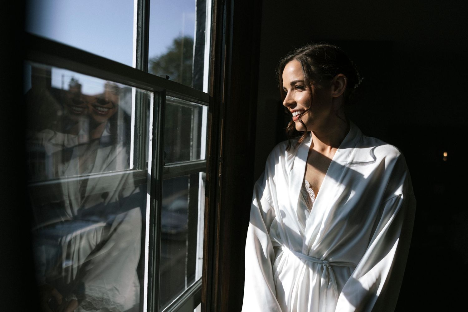 A person in a white robe gazes peacefully through a sunlit window creating a serene morning moment.