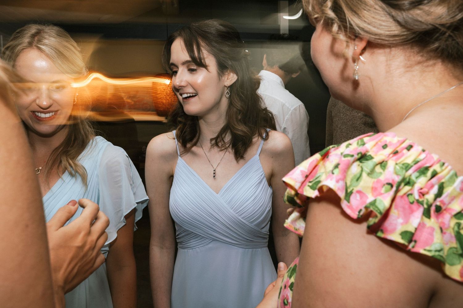Women in elegant dresses laughing together at a wedding reception, bridesmaid in blue gown smiling joyfully.