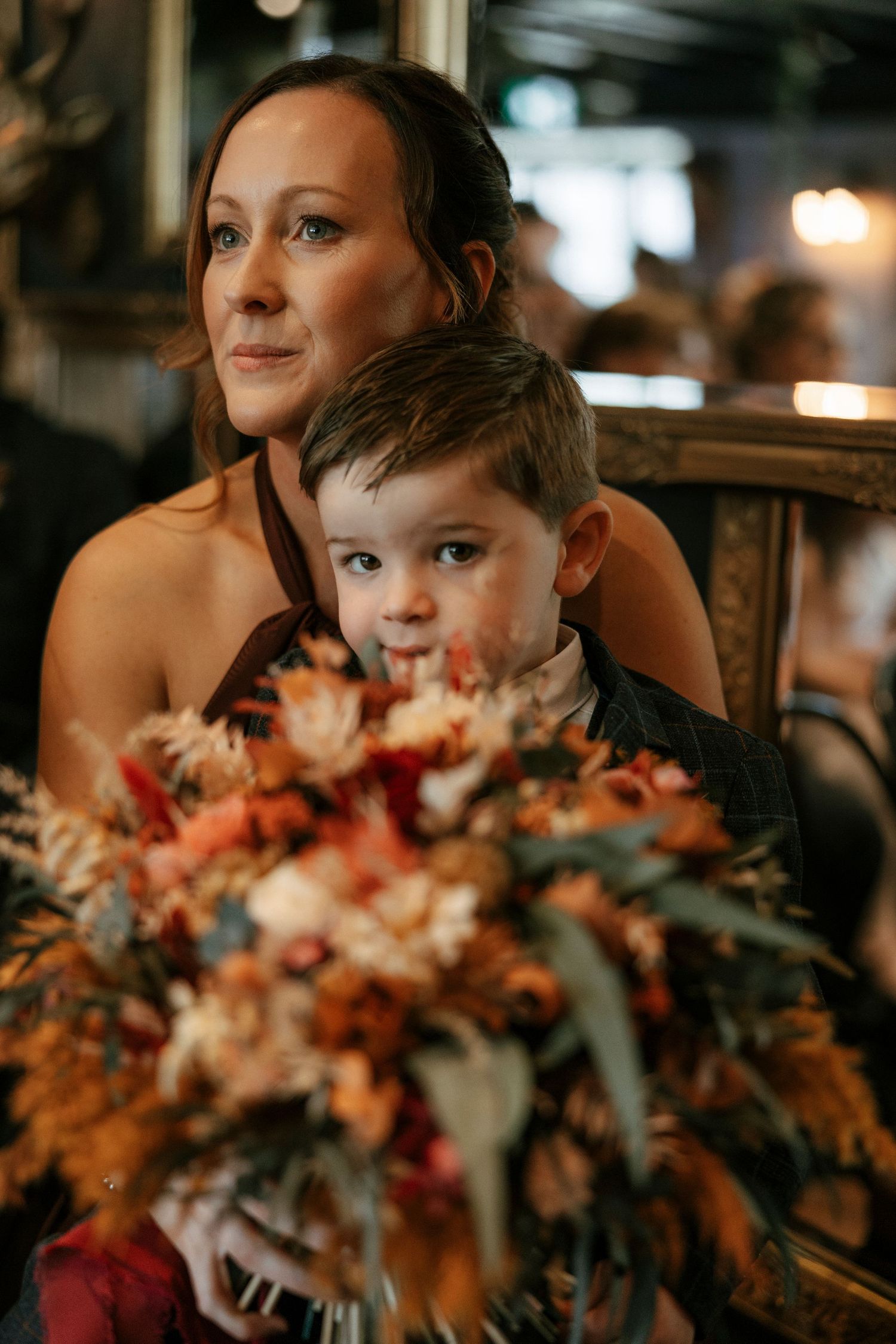 Woman holds colorful autumn bridal bouquet with young boy at wedding reception.