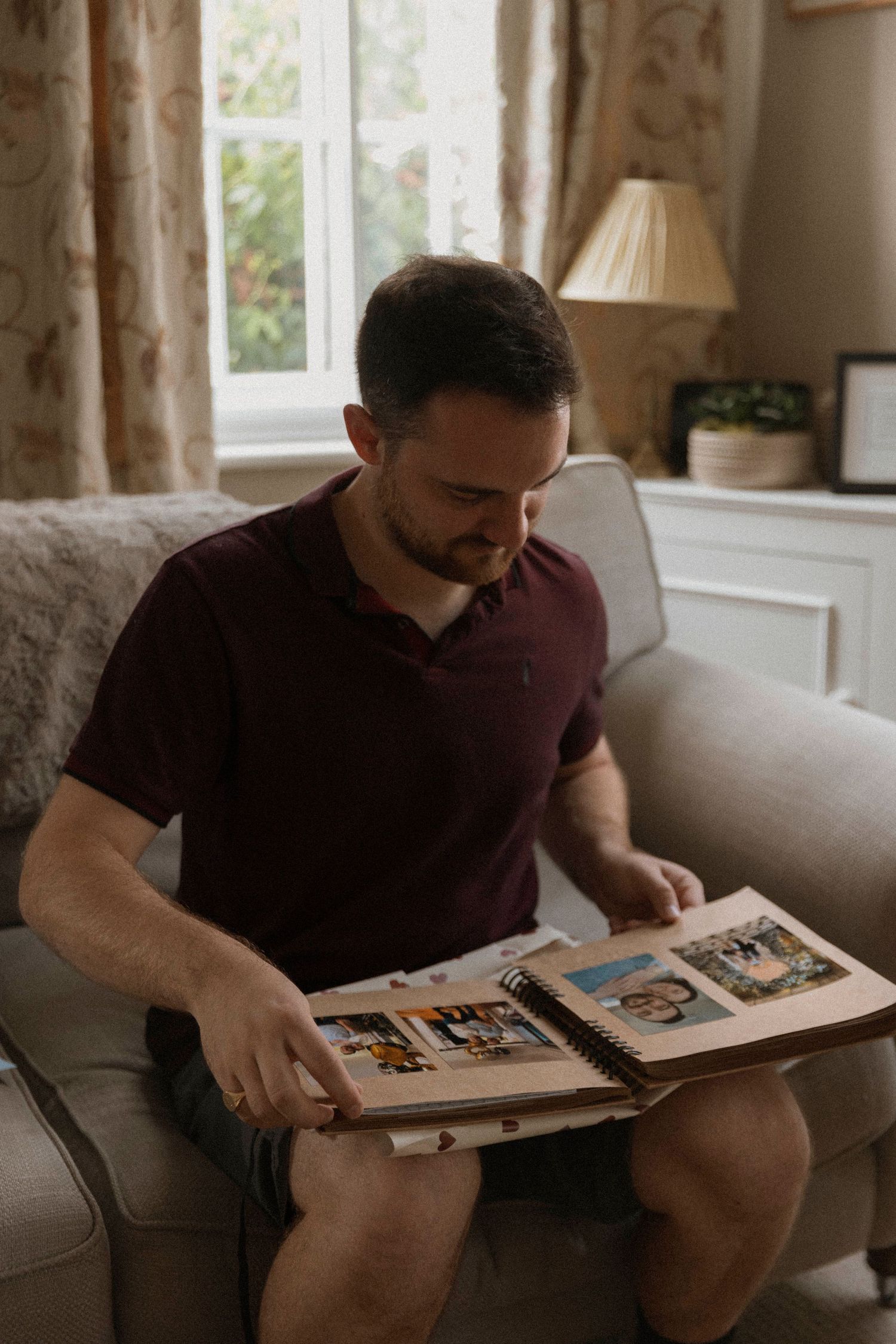 Man in burgundy polo shirt sitting on sofa looking at photo album in cozy living room.
