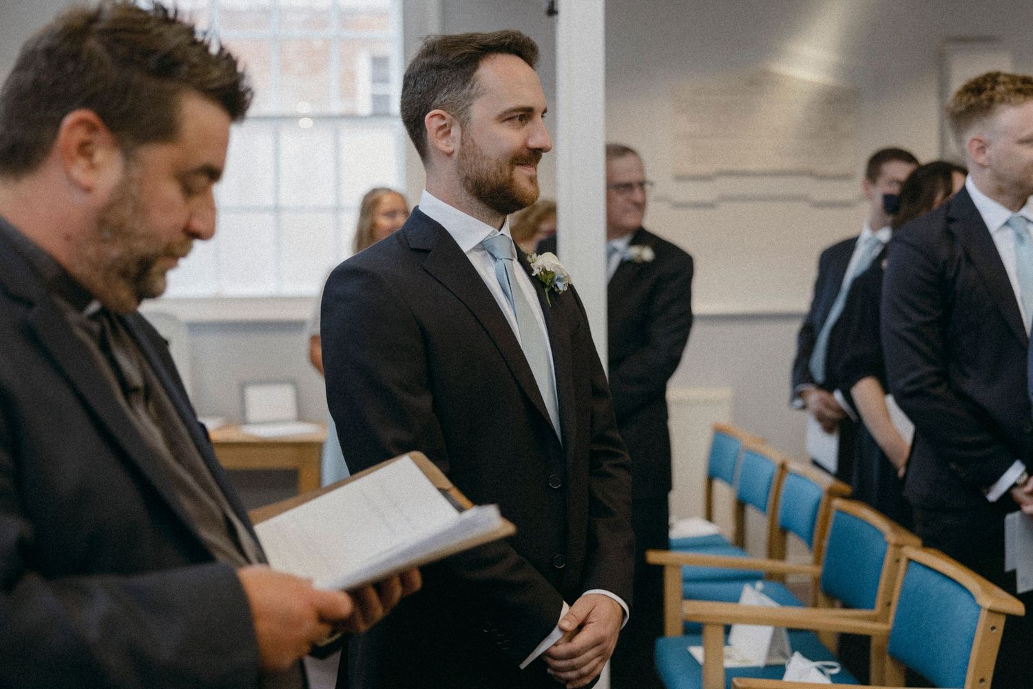 Groom smiling at the altar during a wedding ceremony in a navy suit with a floral boutonniere.