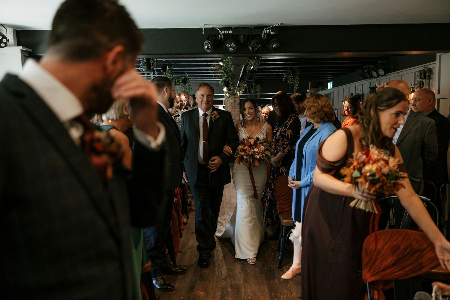 Wedding guests gather in dimly lit venue space as newlyweds make their entrance.