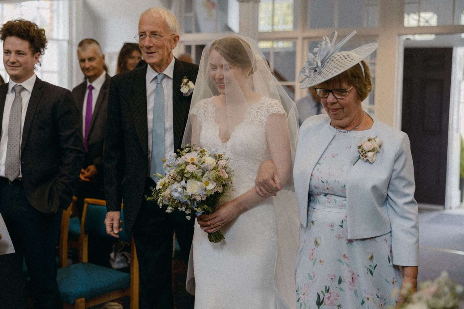 Bride walks down the aisle with elderly parents at an elegant church wedding ceremony.