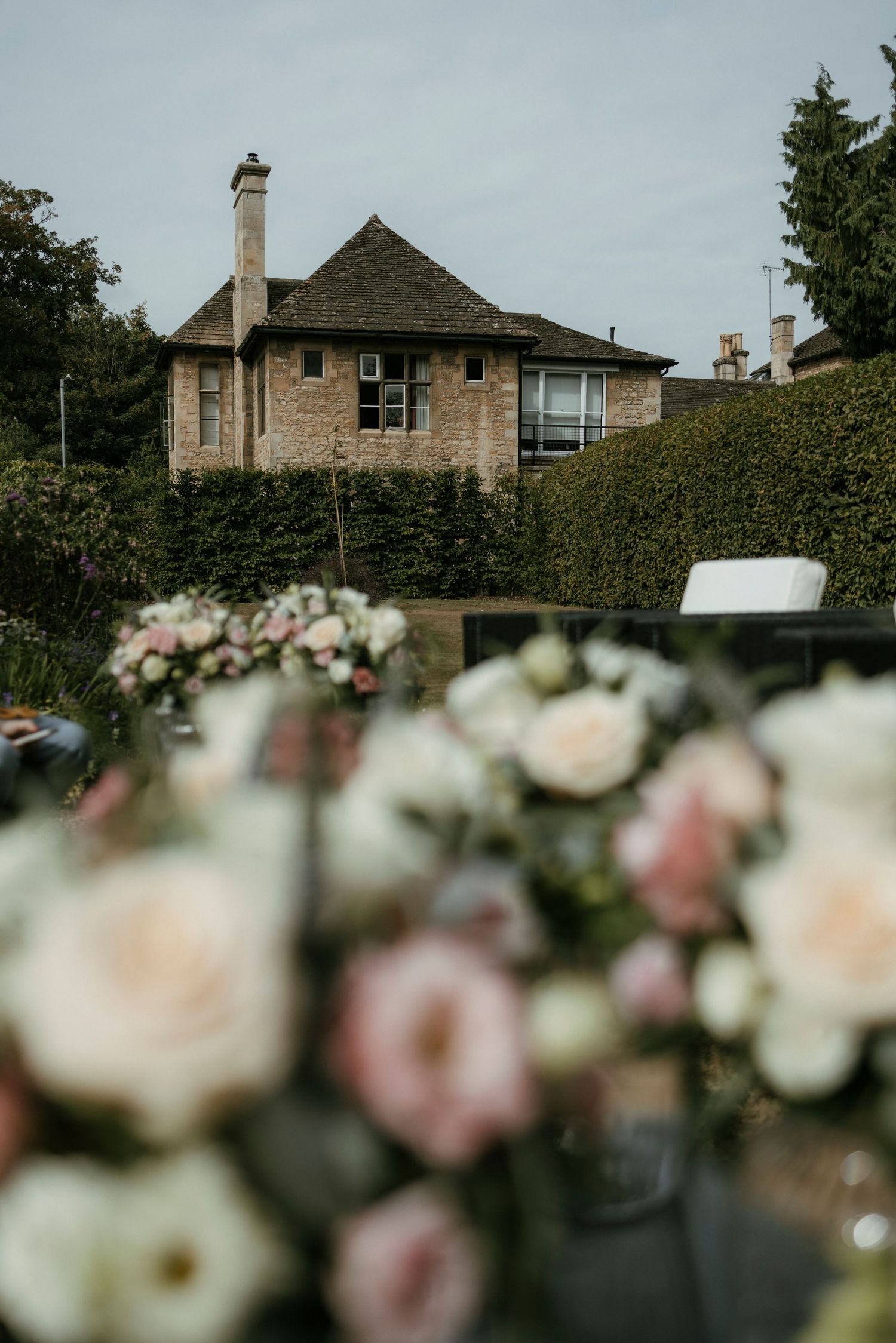 Blurred pink and white floral wedding arch with stone country house venue in background.