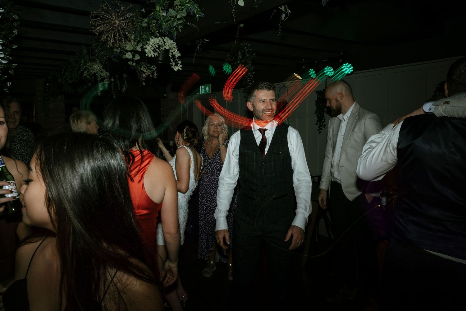 People dancing at dimly lit party with green and red lights overhead.