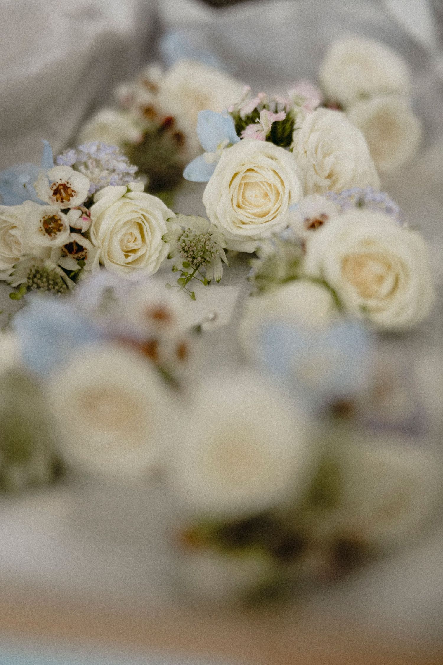 Soft white roses and delicate blue flowers arranged elegantly on a light fabric surface for a wedding.