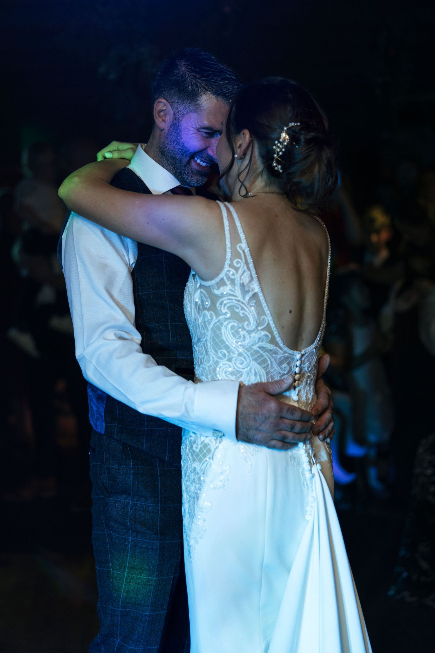 Couple sharing an intimate first dance at their wedding reception, bride wearing elegant lace back dress in evening light.