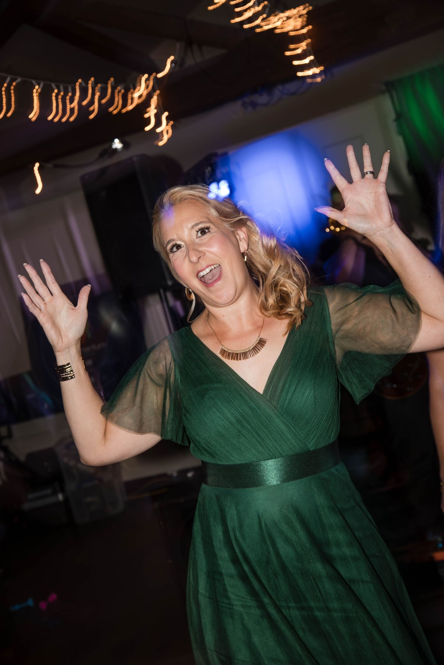 Person in emerald green dress dancing enthusiastically at a party with blue lighting in the background.