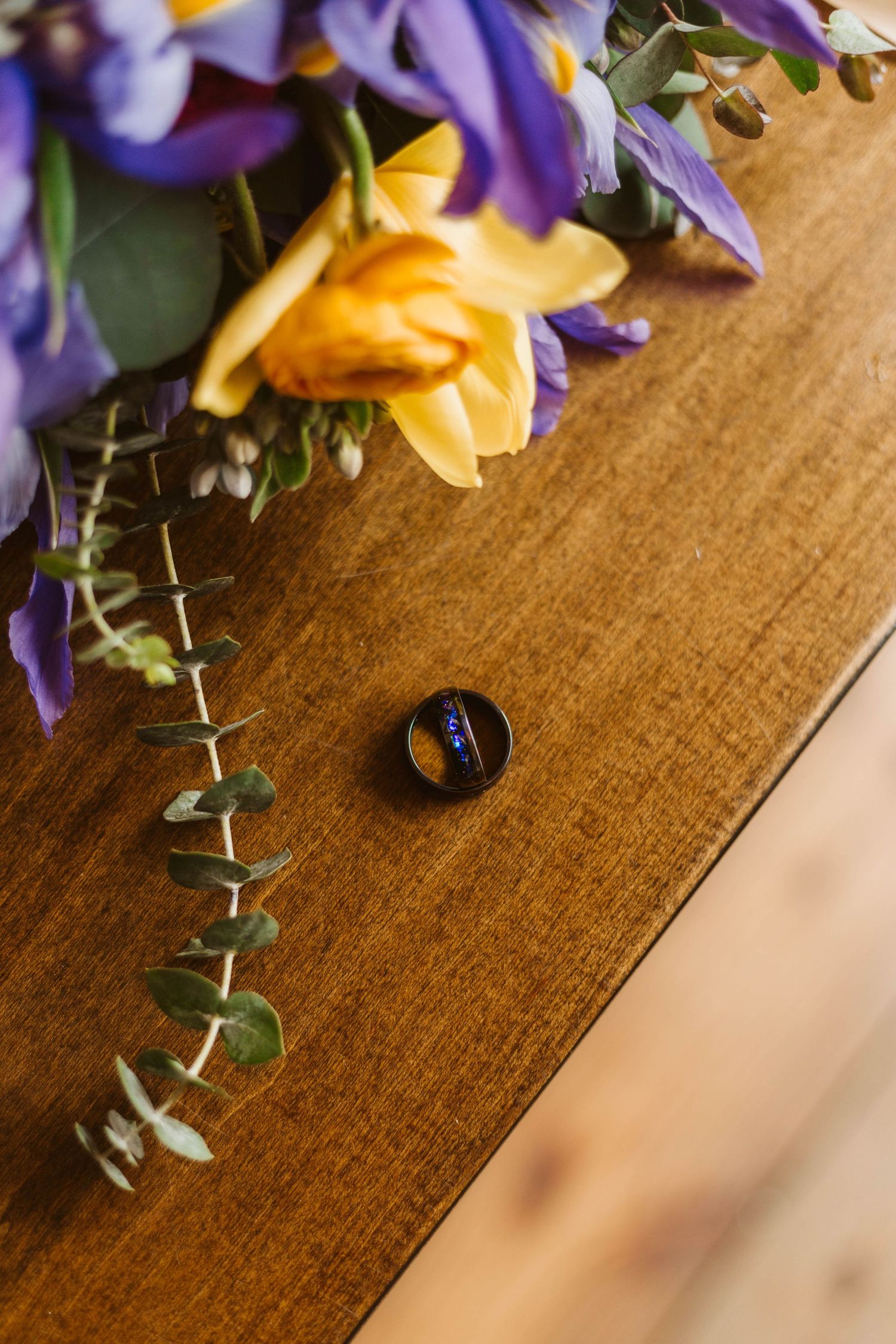 Ring against light wood next to yellow and purple flowers
