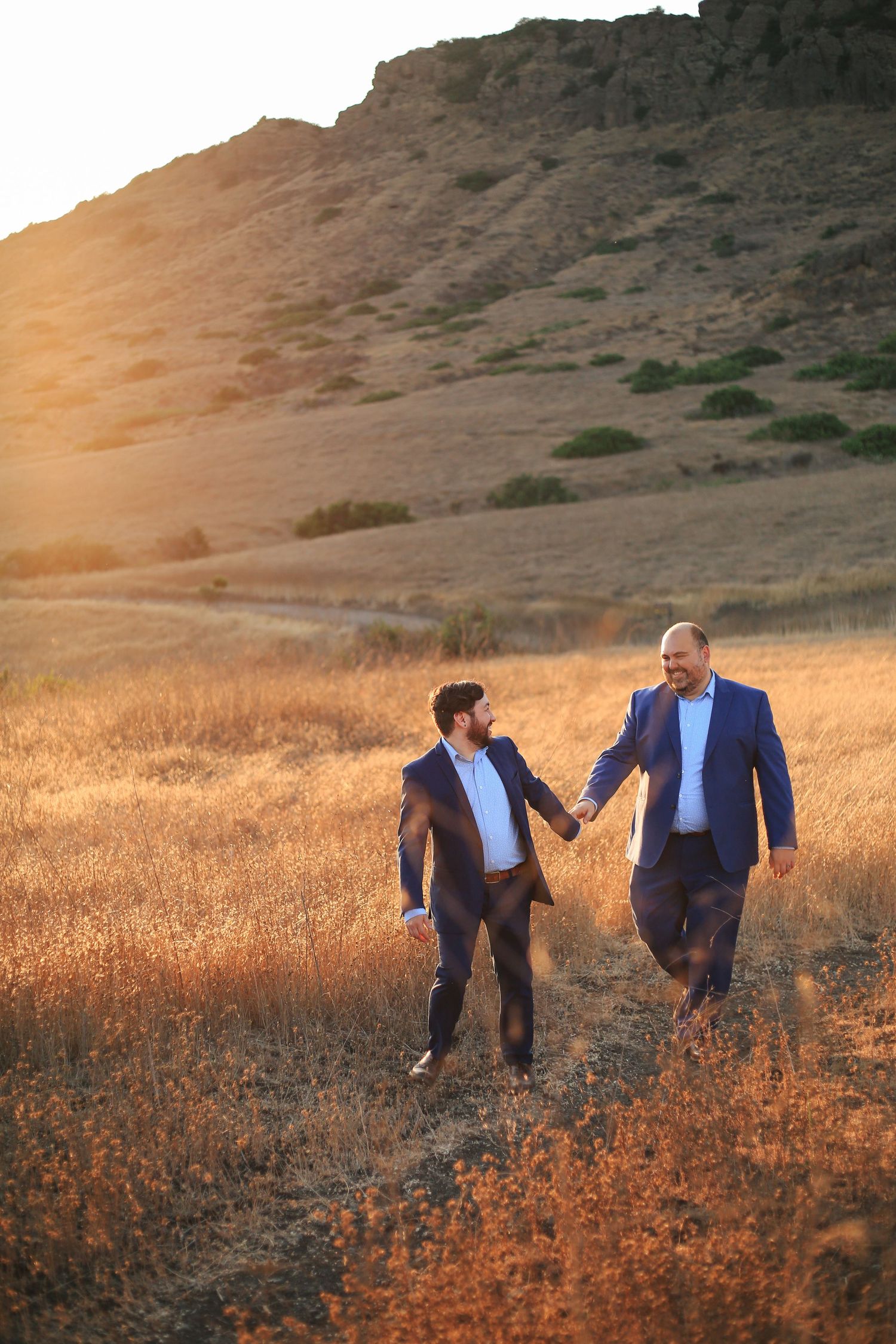 Engaged couple holding hands while walking through a golden field at golden hour