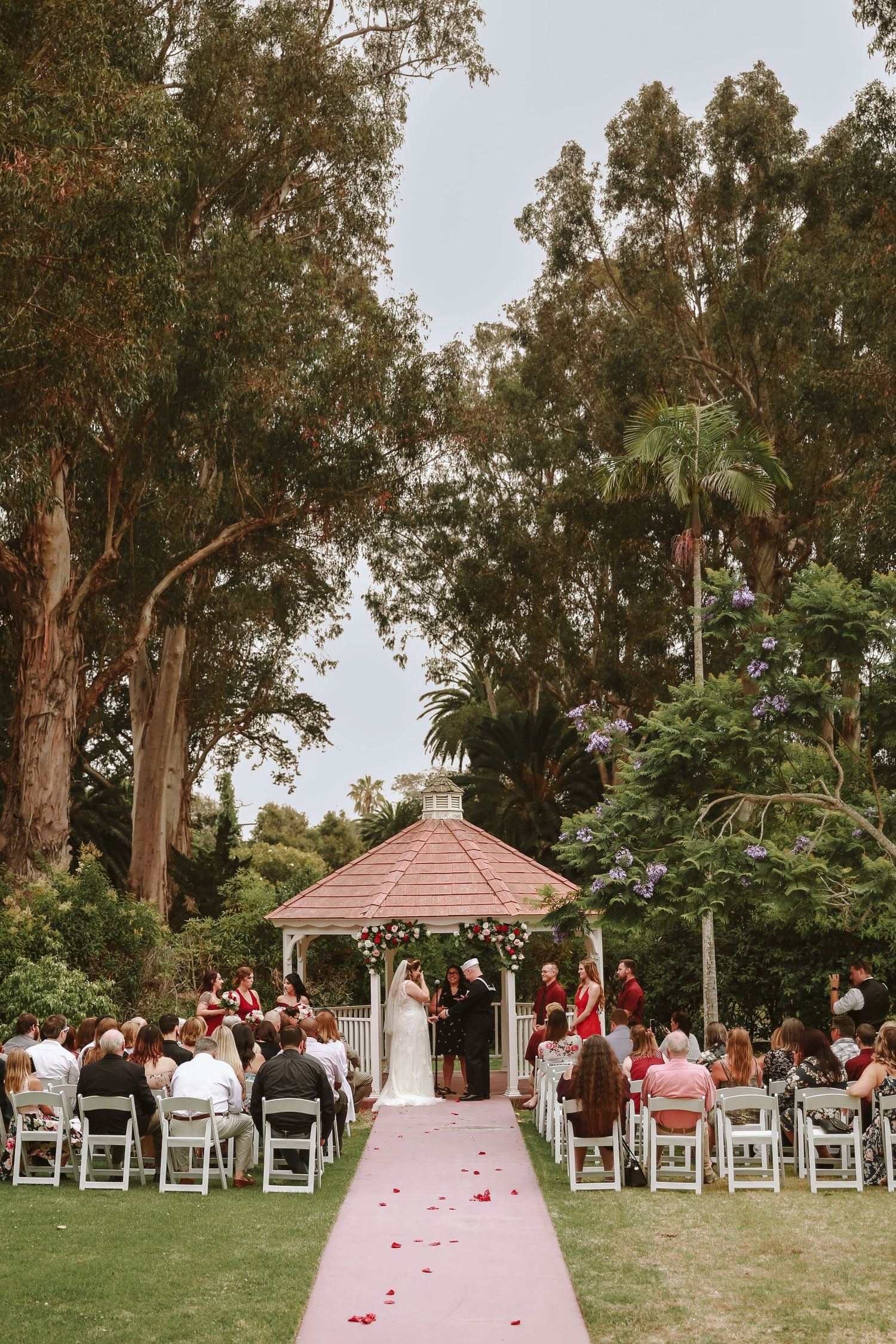 Gazebo with a Bride and Groom standing in front of their audience outside with lush trees behind them