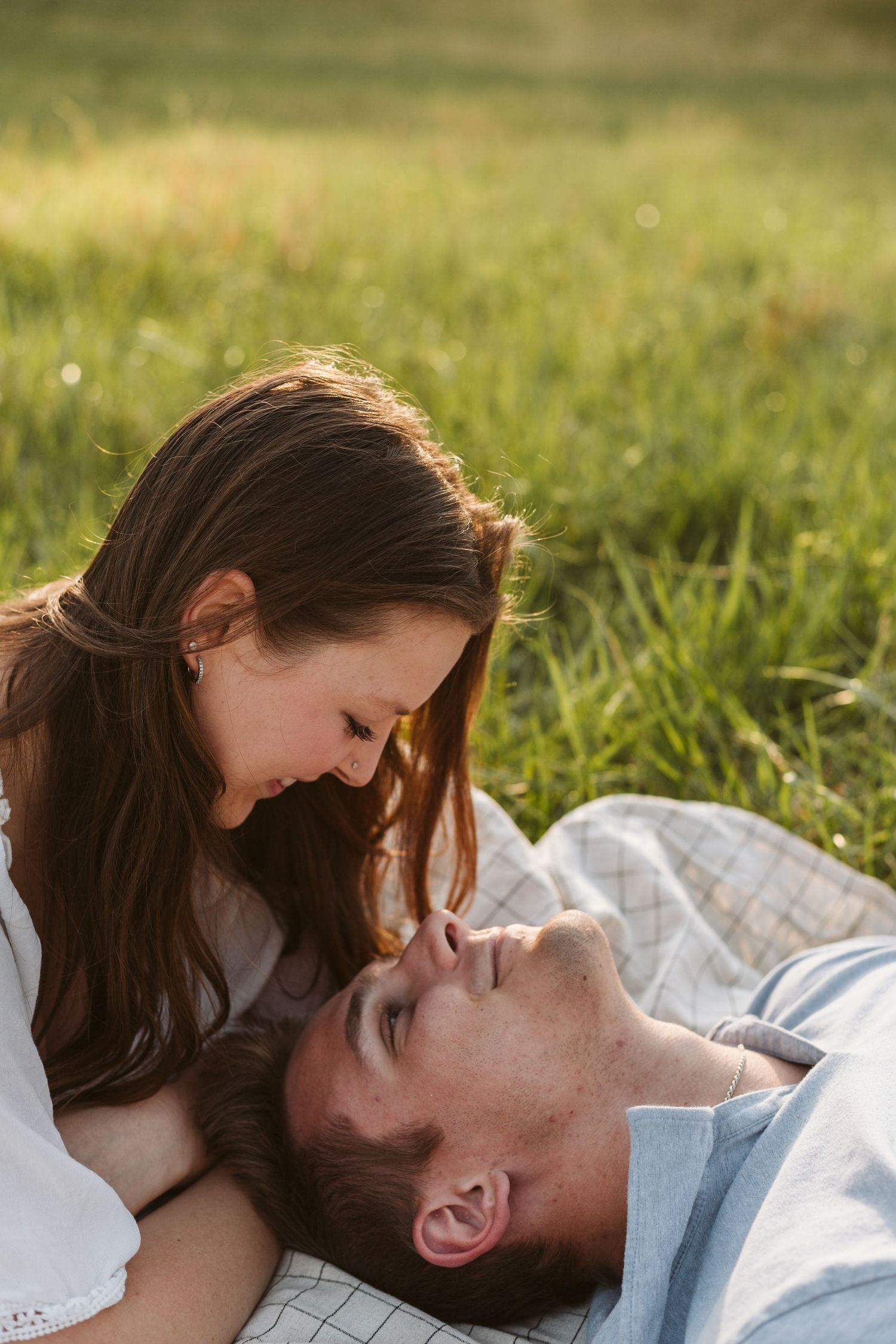 Couple laying on a blanket in a field gazing into each others eyes
