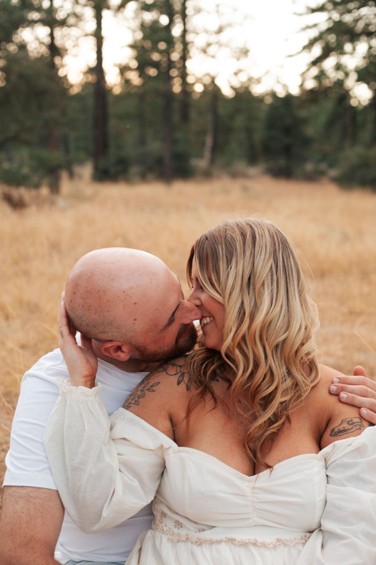 Woman in a white dress kissing her fiancee on a blanket in a field