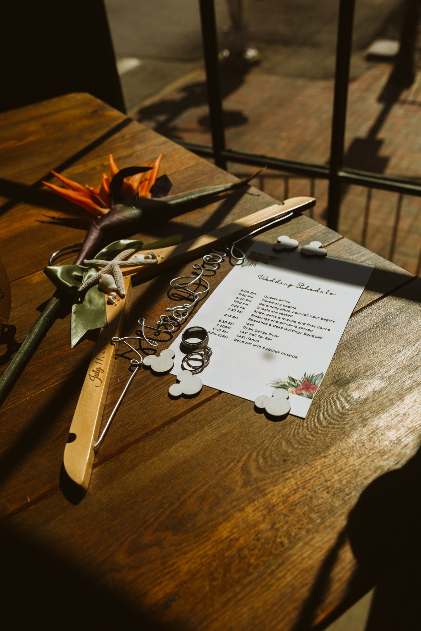 Details of the invitation, rings, flowers, and hangar on a wooden table in the shadow of the window