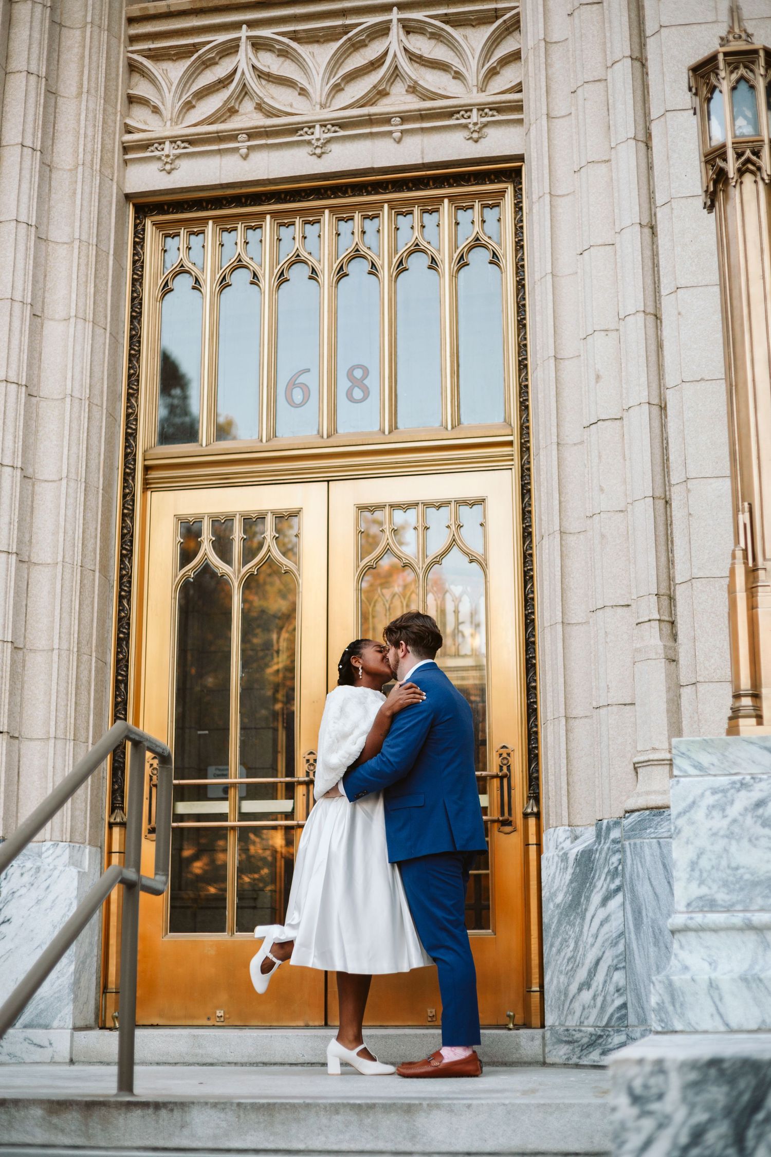 Bride and Groom sharing a kiss infront of stunning golden doors with complex metal work and glass