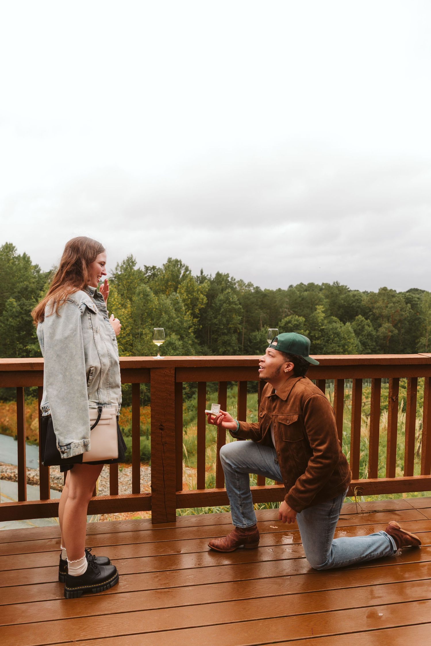 Man purposing on one knee to a woman near railing