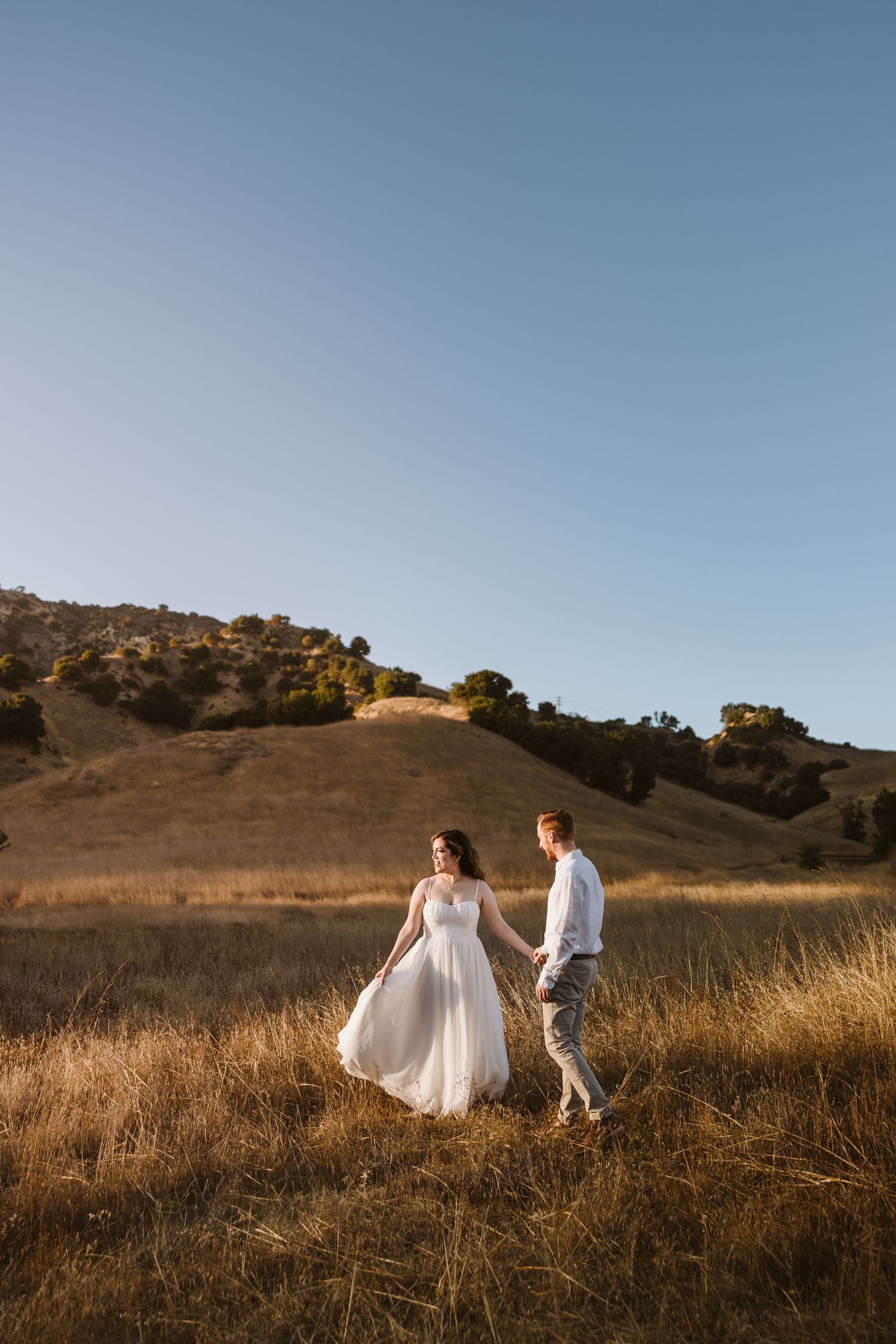Engaged couple walking through a dry field in Malibu Creek at sunset