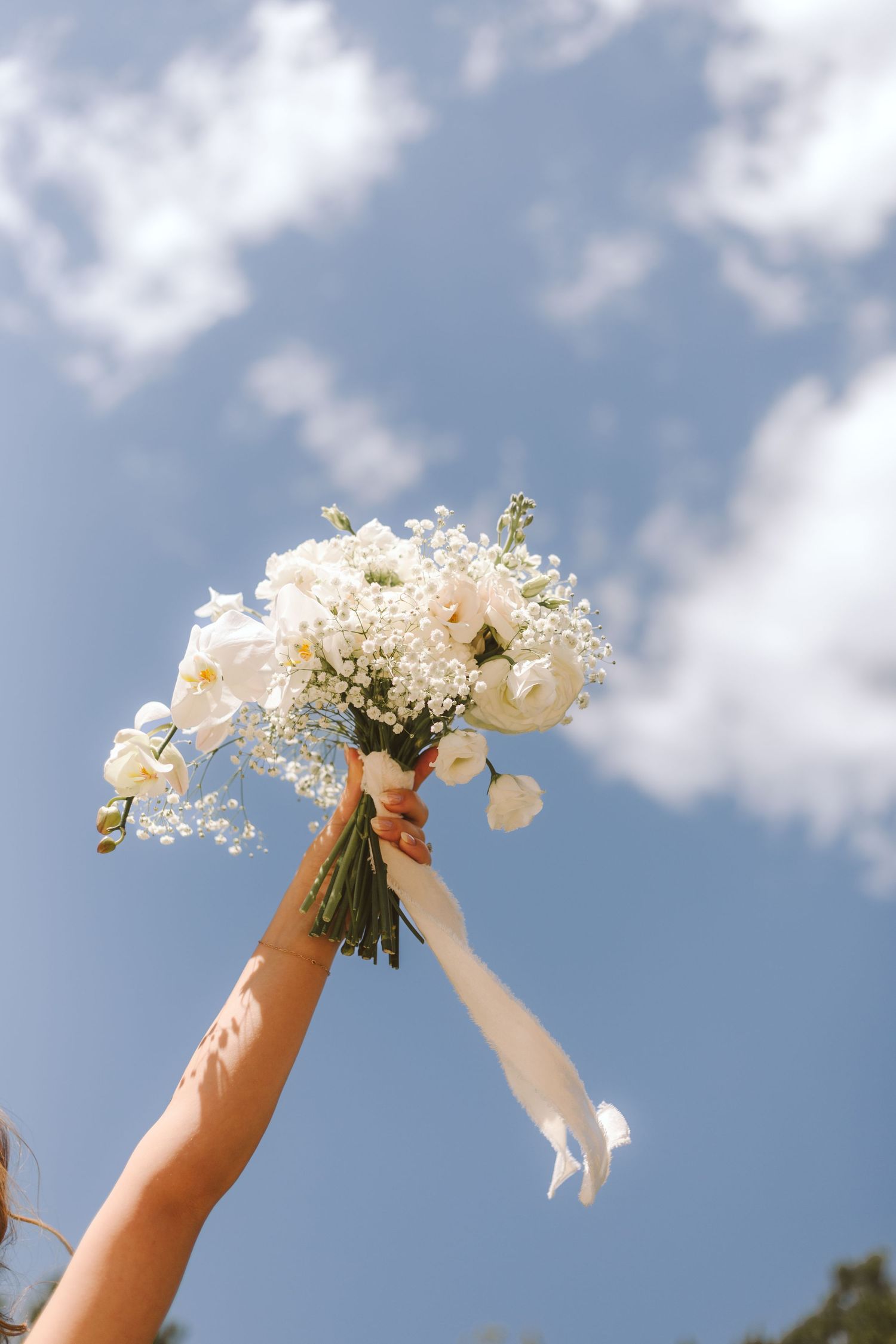 Bride holding her bouquet up against the blue sky with scattered clouds
