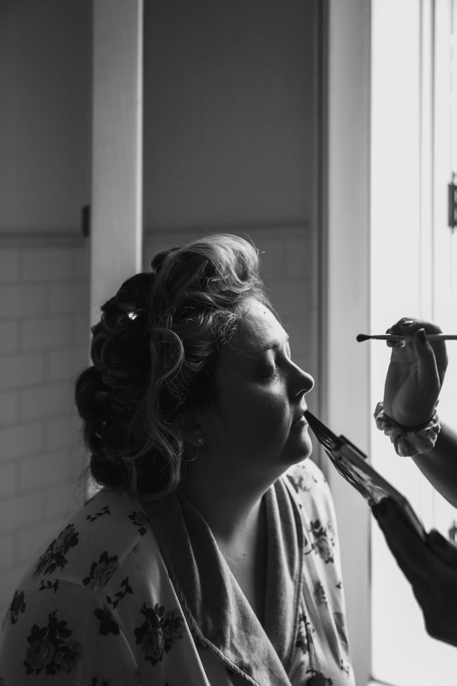 Bride with curlers getting ready for her wedding having her makeup applied (black and white)