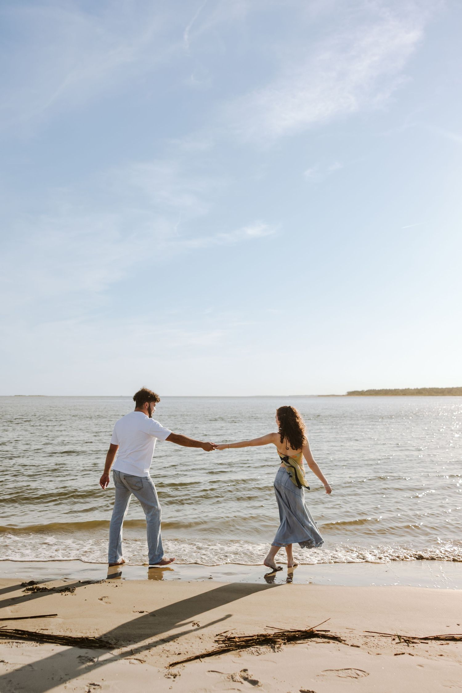 Couple stretched out to hold hands while walking along the shore