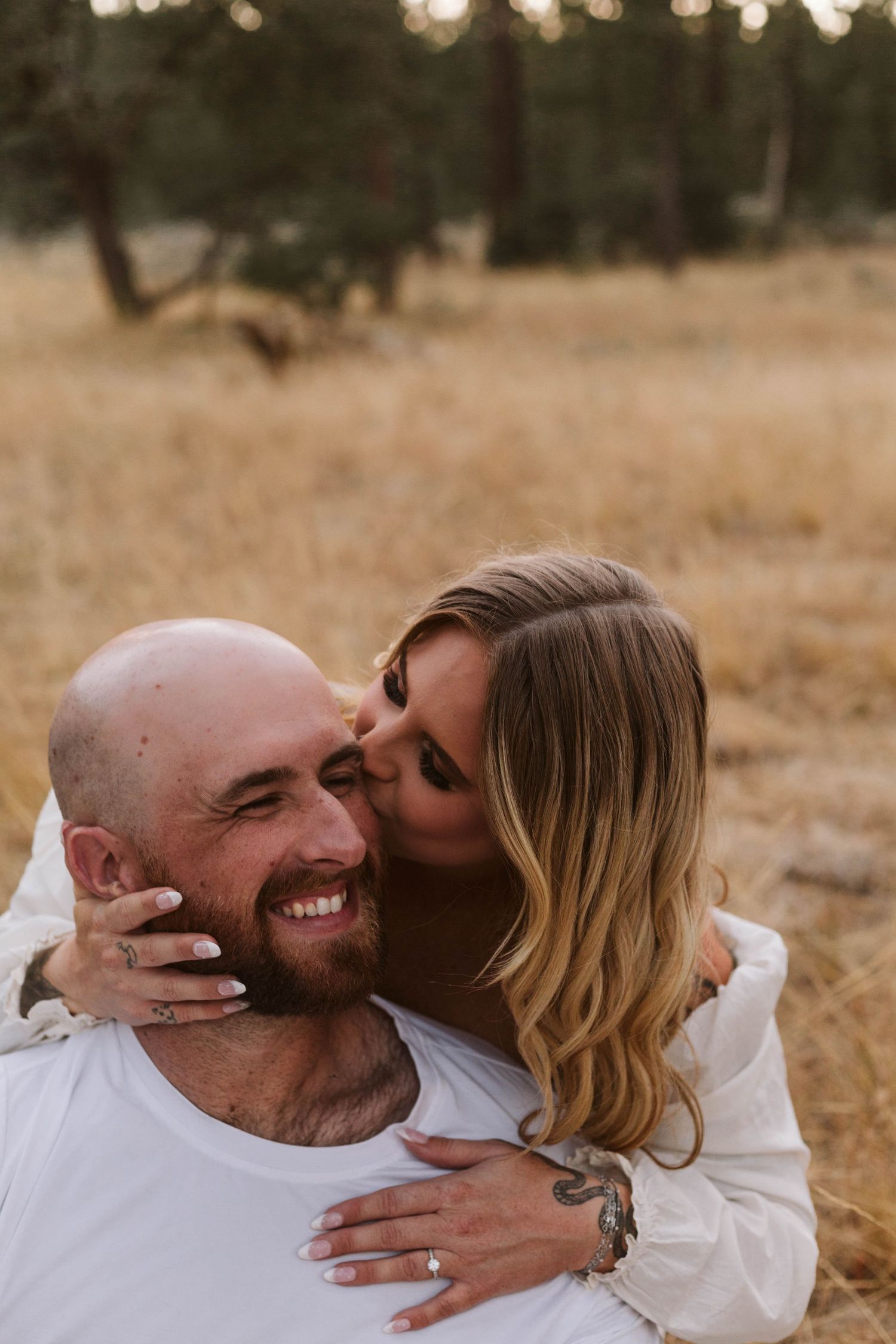 Blonde hair woman kissing her fiancee on the cheek in a field