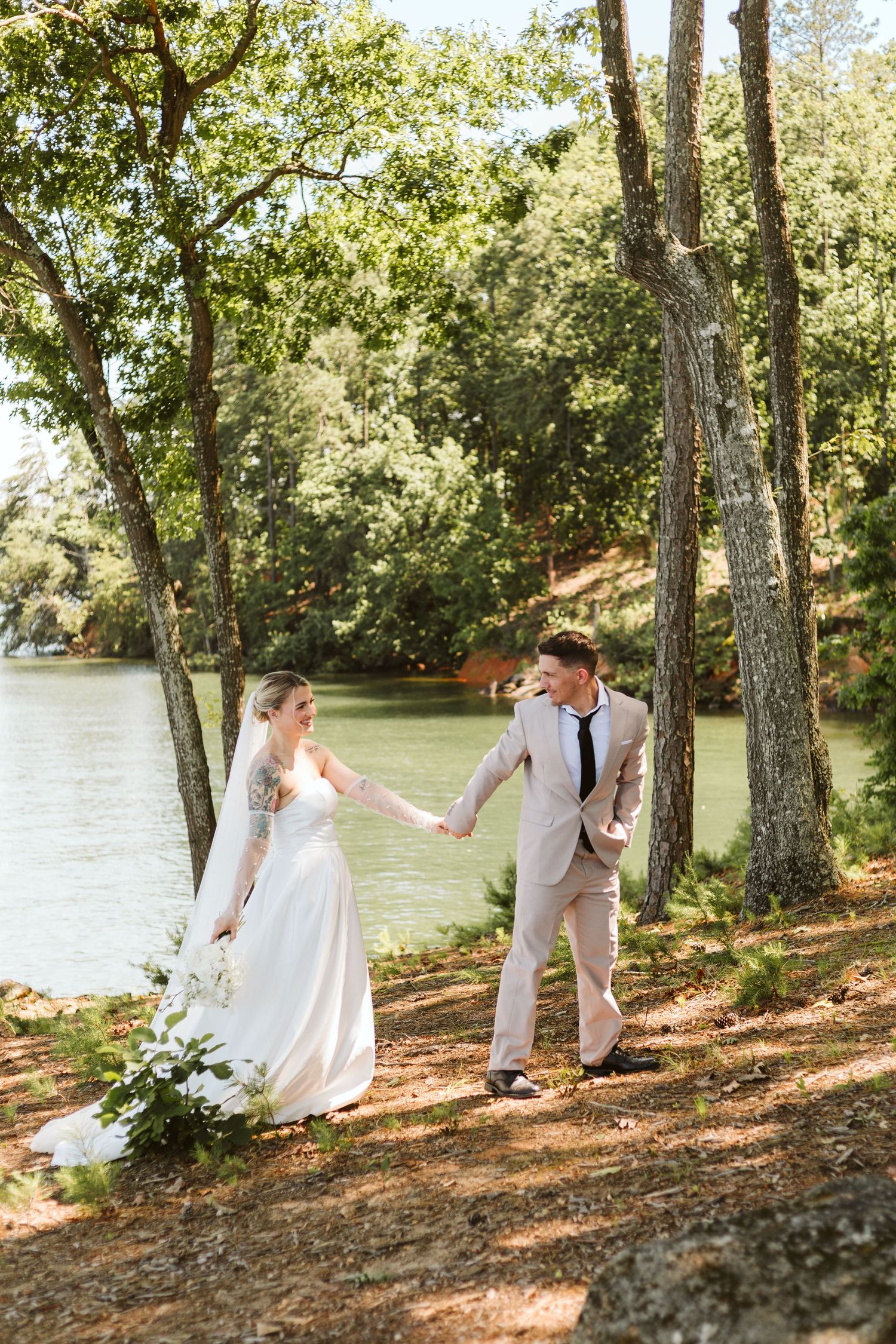 Bride and groom holding hands while walking through the woods near a lake