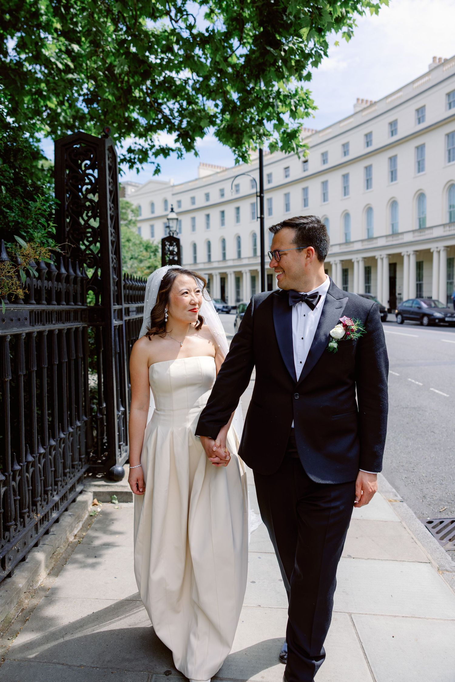 Bride and groom walking hand in hand past elegant white Regency buildings in London.
