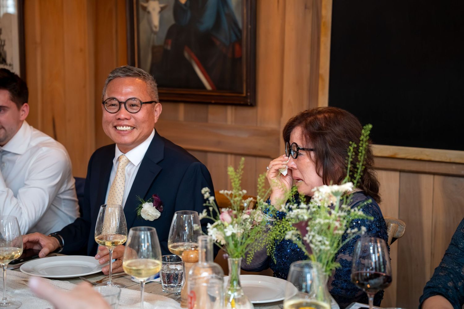 Guests laughing and smiling during a wedding reception dinner at a rustic venue.