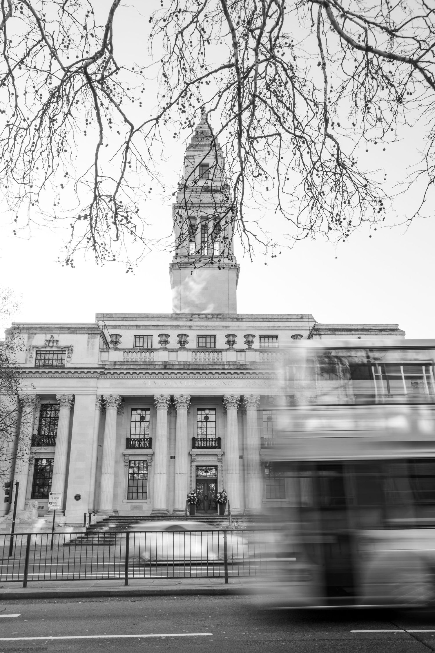 Motion-blurred vehicles pass by a stately white government building with classical architecture and columns.
