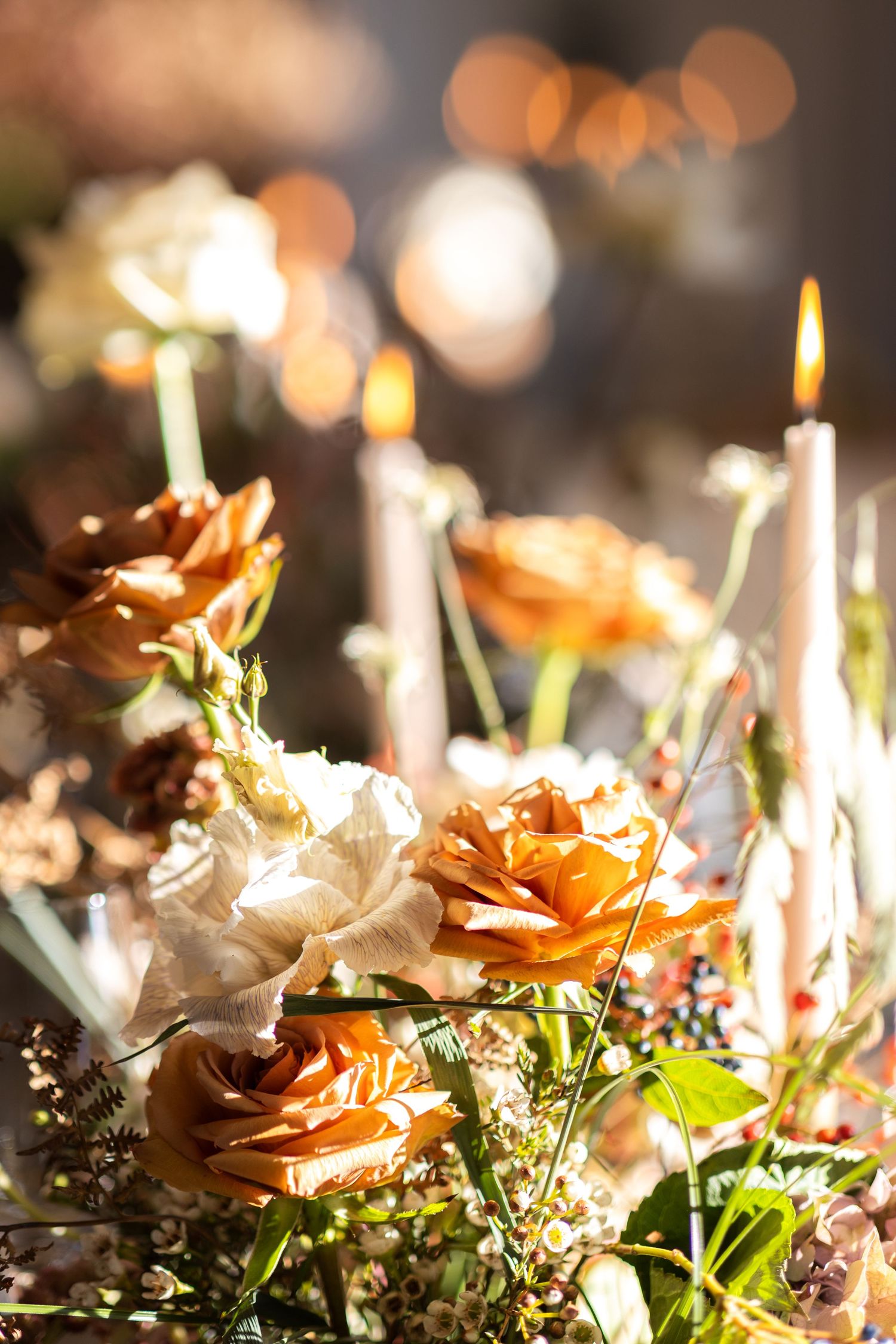 Romantic candlelit table setting with orange roses and delicate floral arrangements creating a warm ambiance.