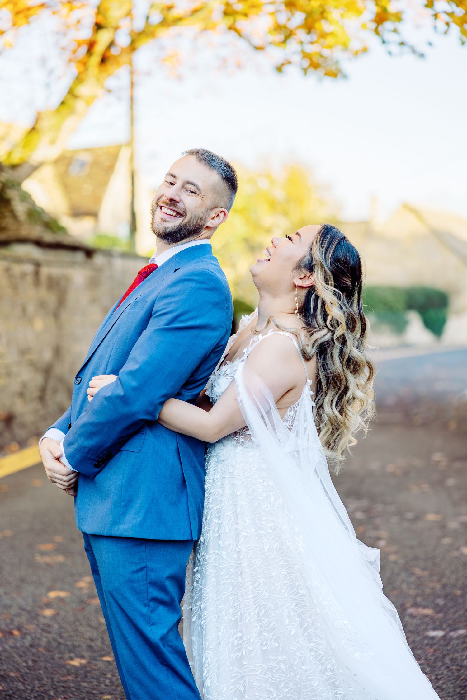 Playful wedding couple laughing together under yellow fall foliage.