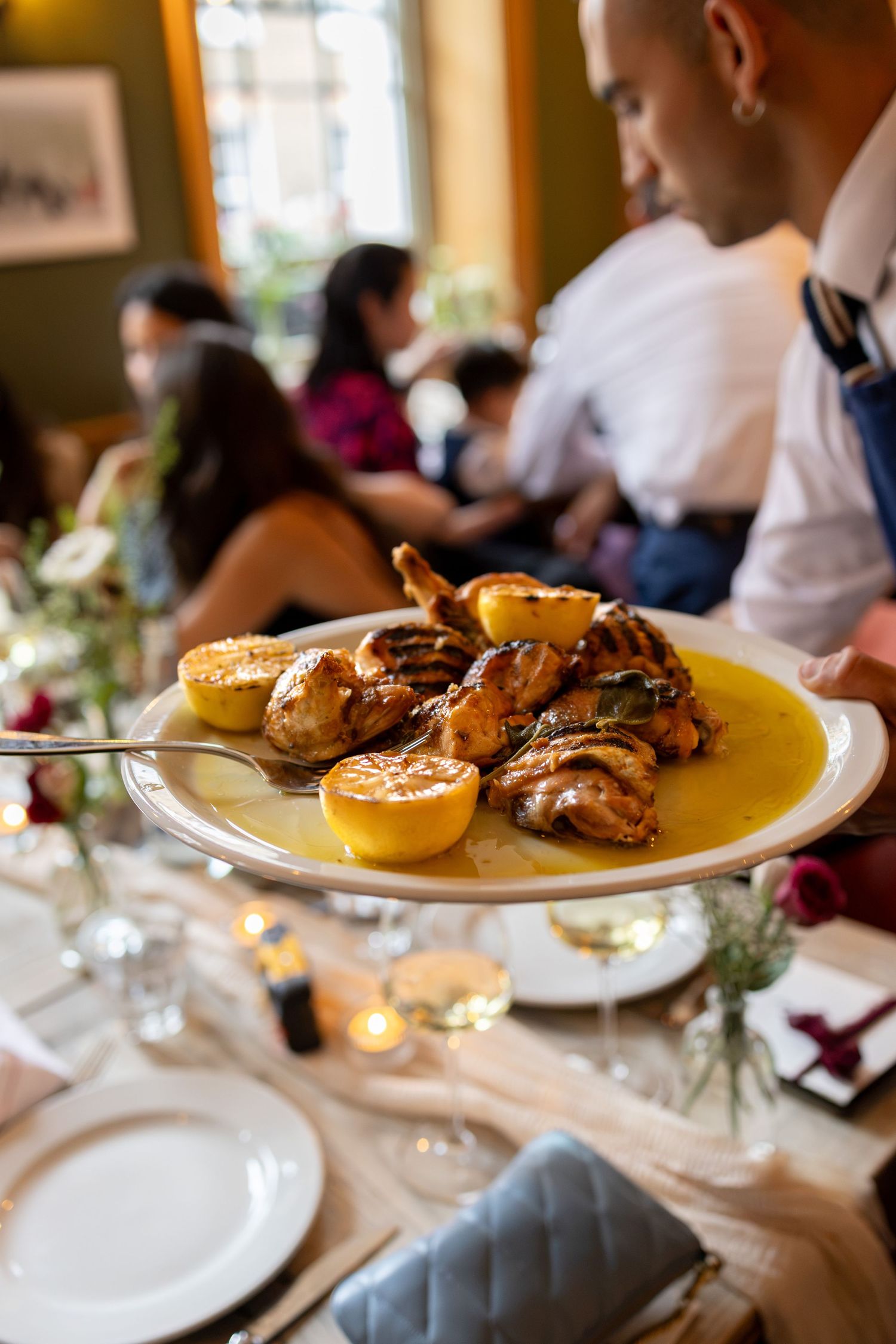Server presents roasted chicken dish with lemon garnish to guests at wedding reception dinner.