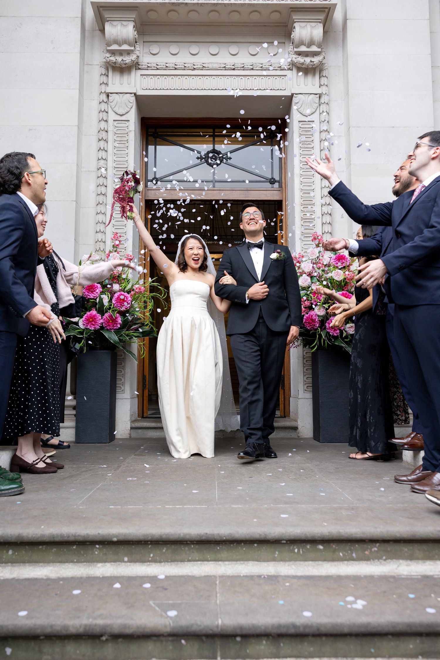 Newlywed couple exits church doors as guests toss confetti in joyful wedding celebration.