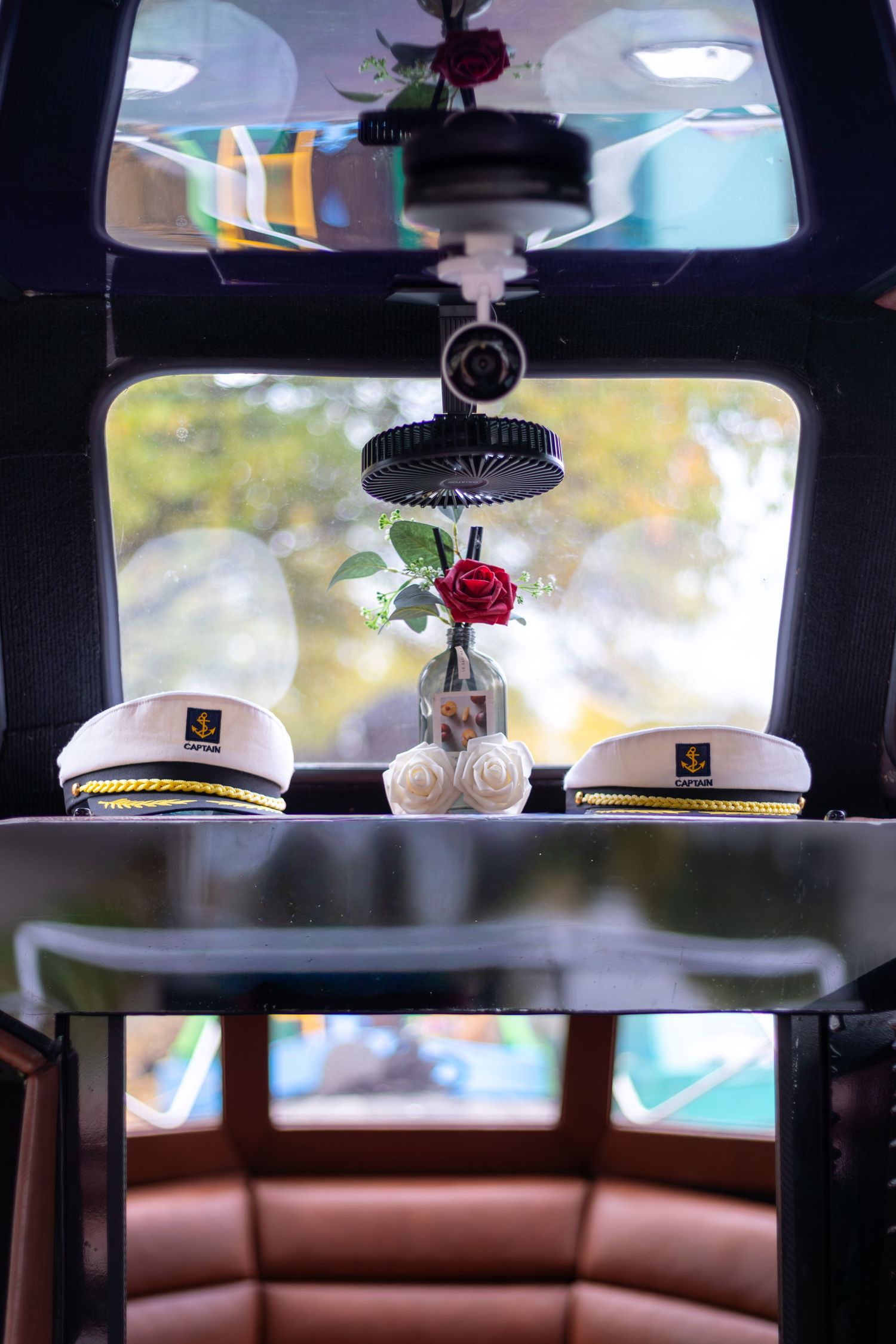 Two white naval captain hats with black brims sit on a car dashboard with a small red rose between them.