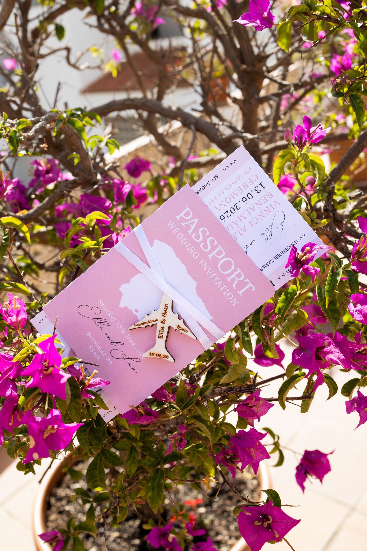 Passport-style wedding invitation tucked in vibrant pink bougainvillea flowers on a sunny day.