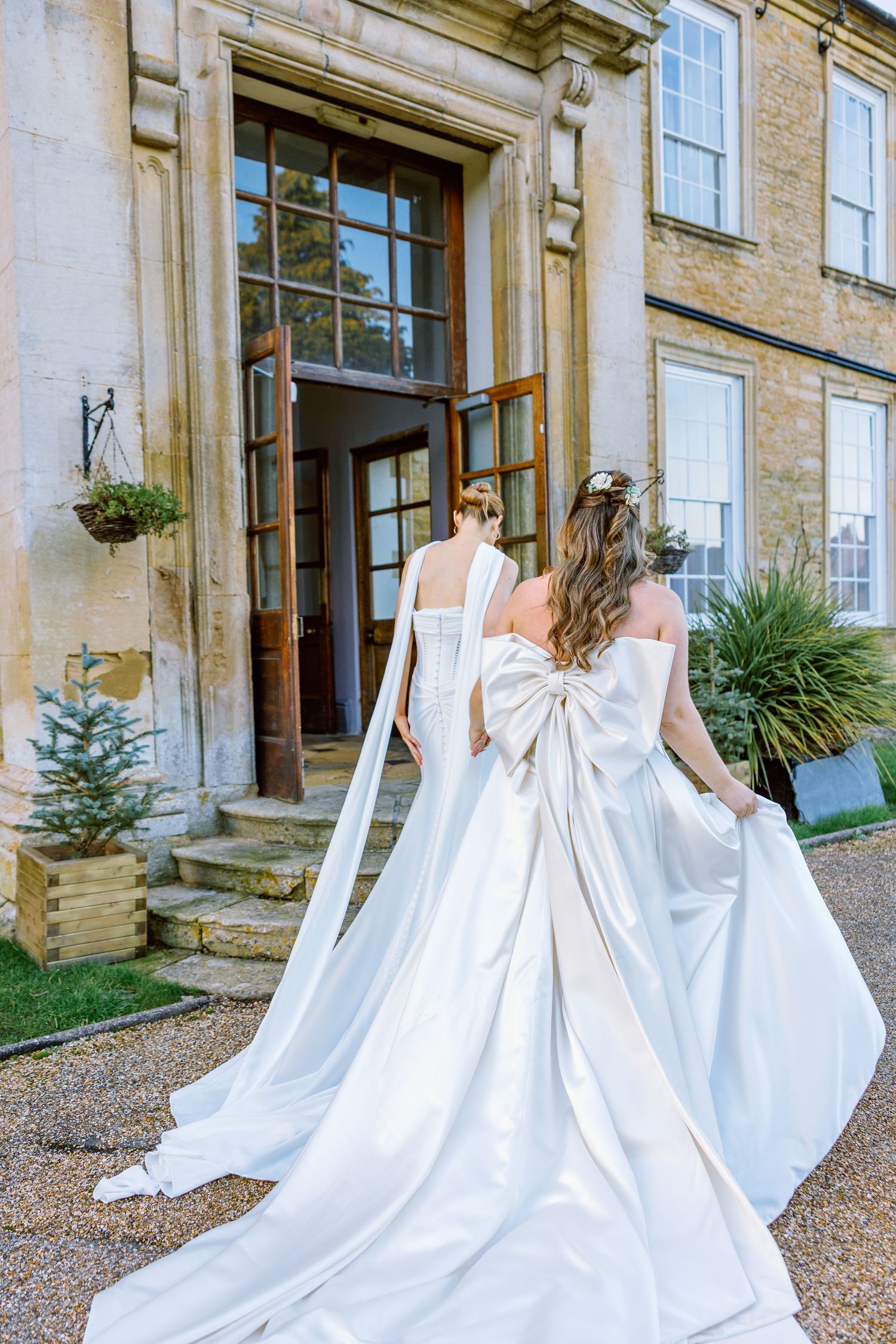 A flowing white wedding gown with a large bow detail photographed outside a historic stone building.