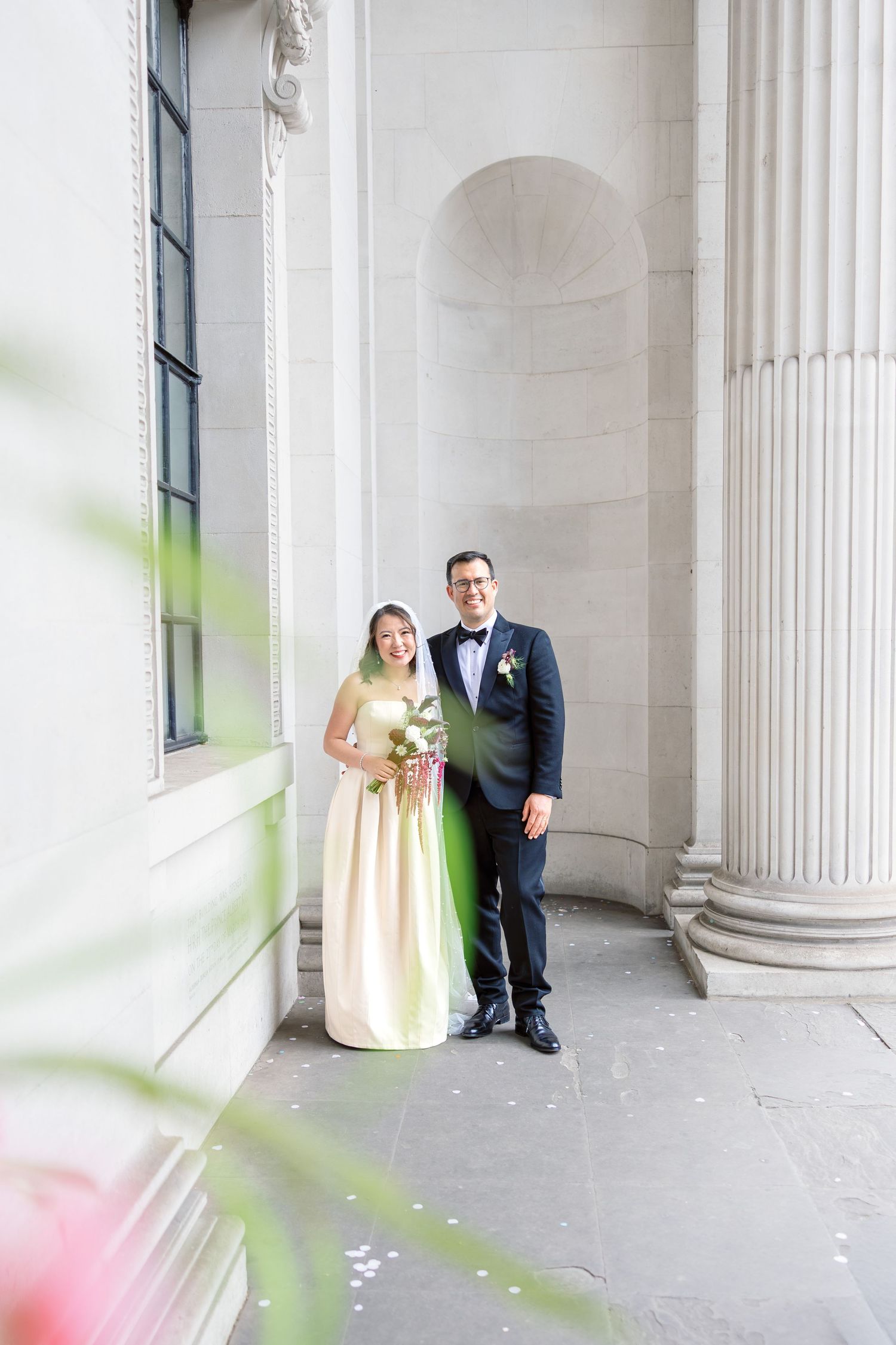 Bride and groom posing between elegant stone columns at a wedding venue.