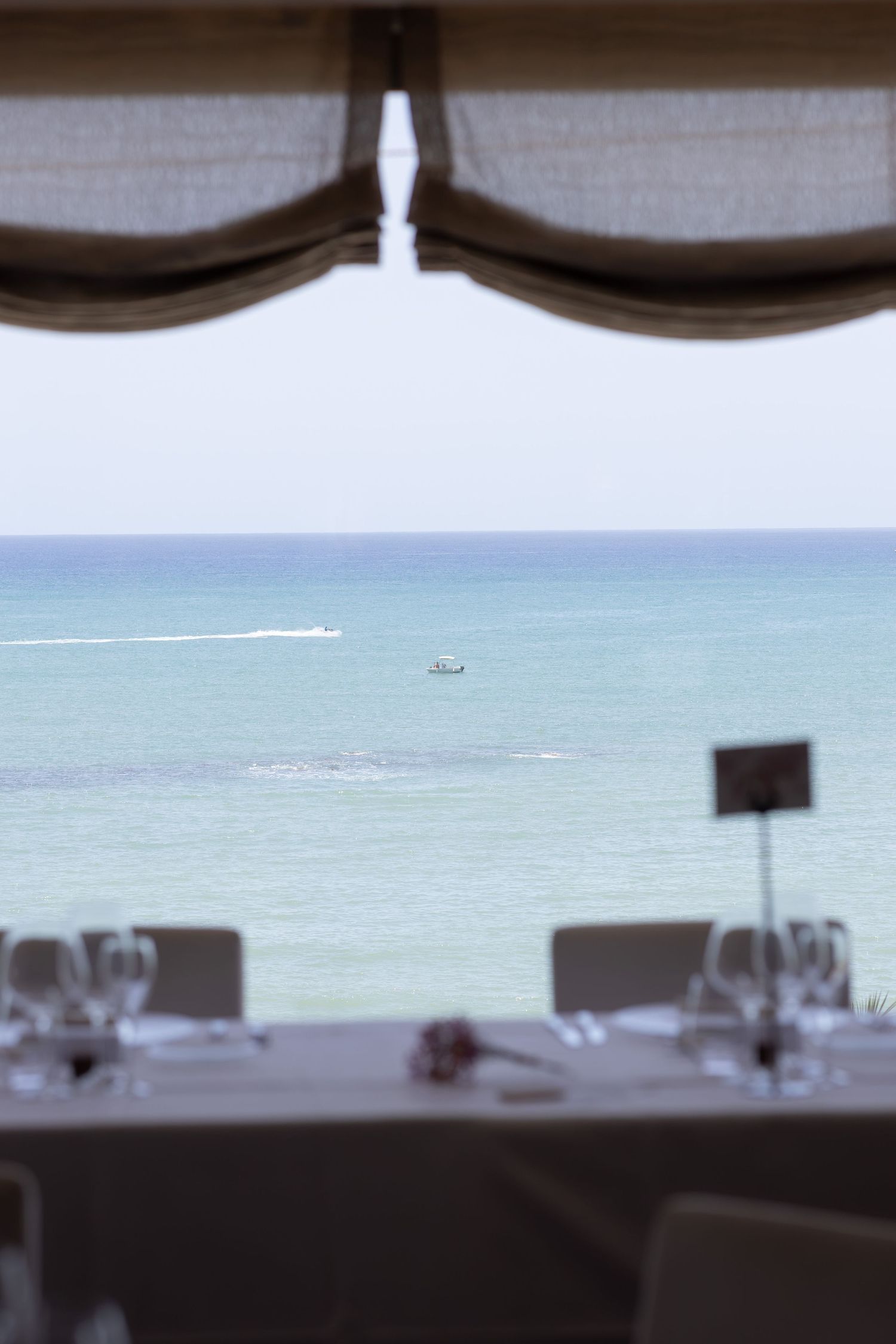 A serene oceanview restaurant table set with glassware framing boats on calm turquoise waters.
