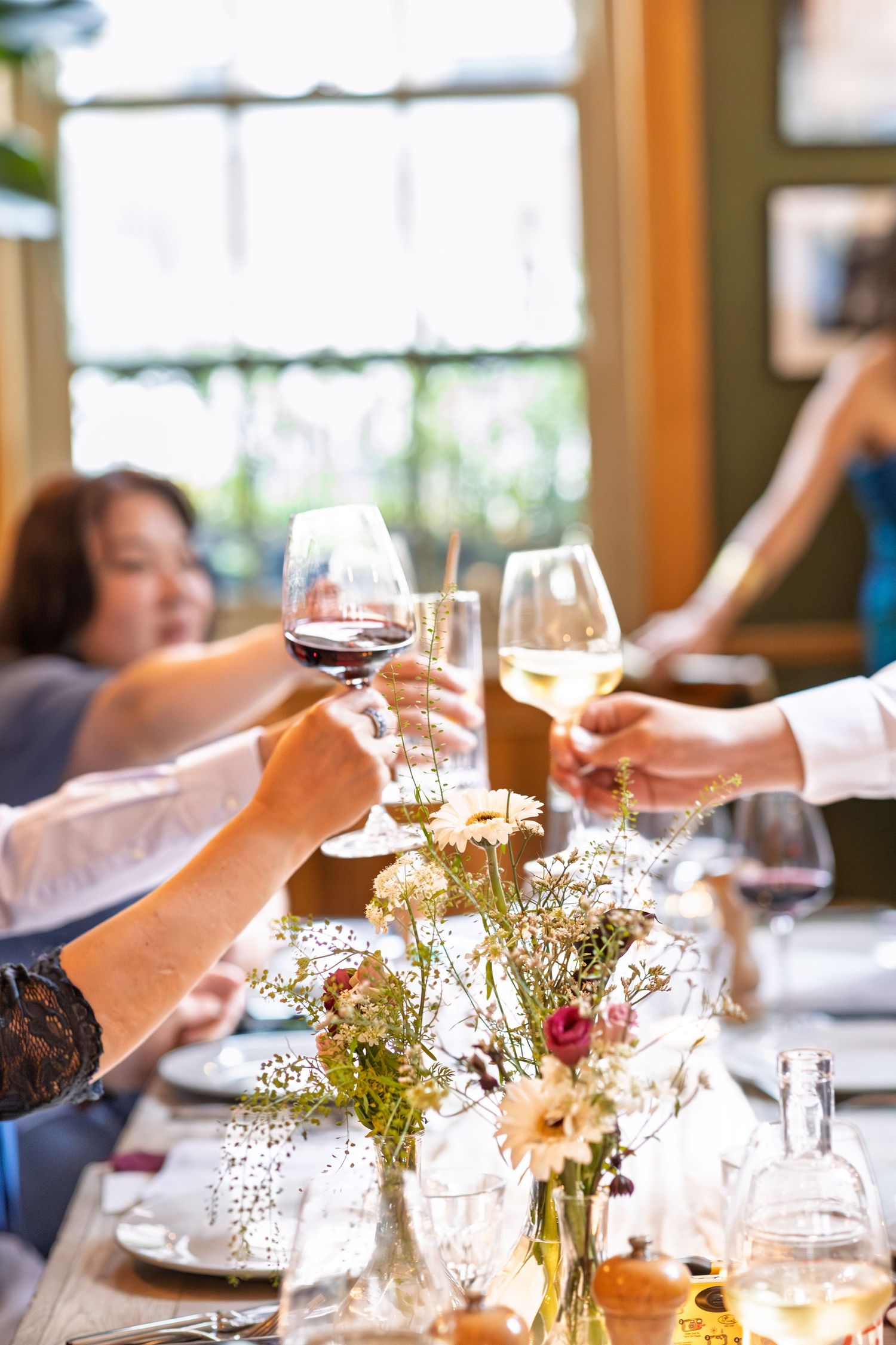 Wedding guests clink red and white wine glasses in a celebratory toast over floral table.