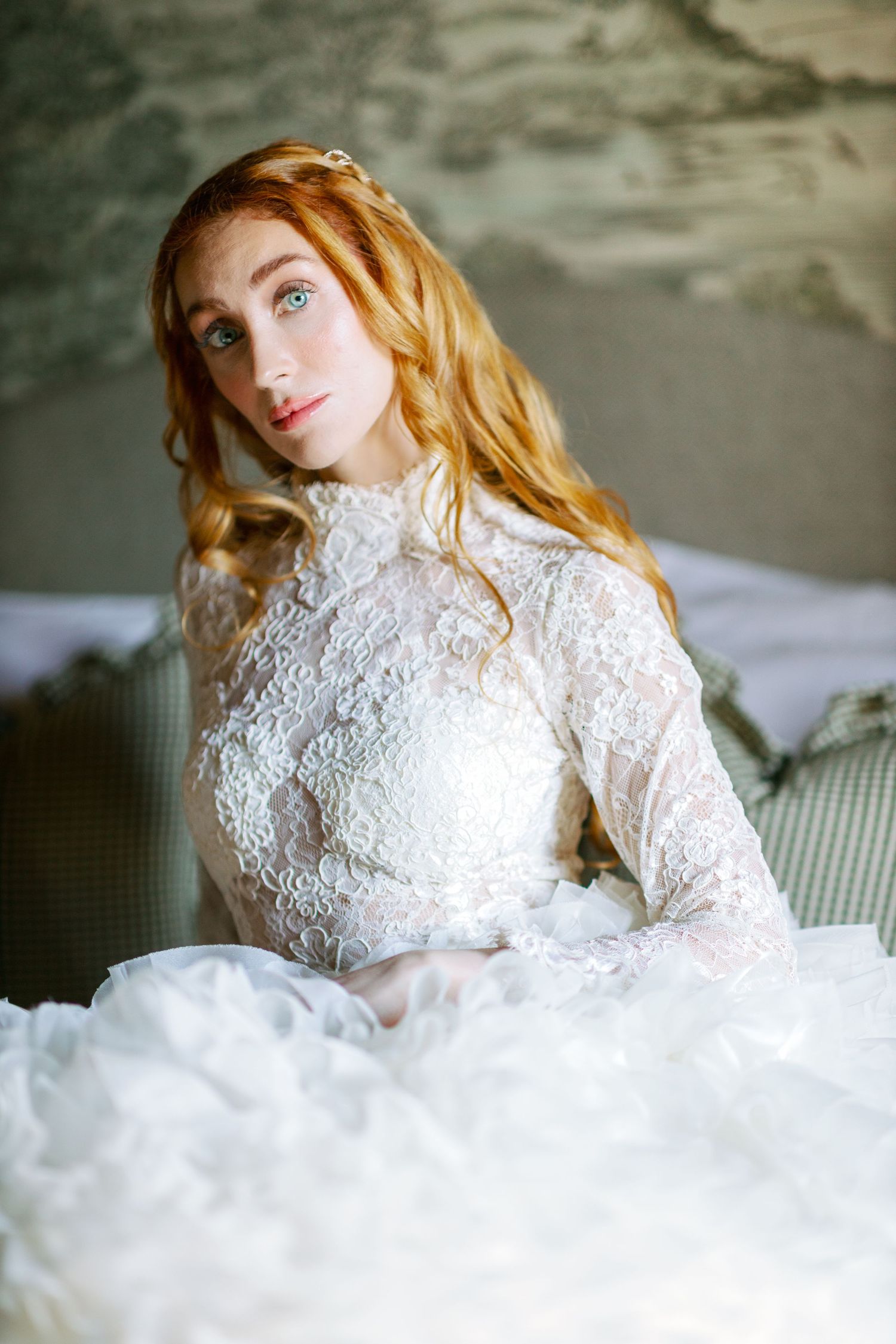 Ethereal bridal portrait with lace wedding gown against textured grey background.