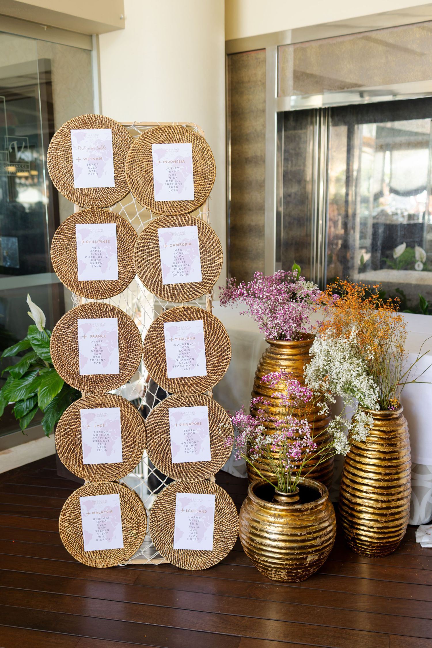 Decorative seating chart display with woven circular frames and golden vases with flowers.